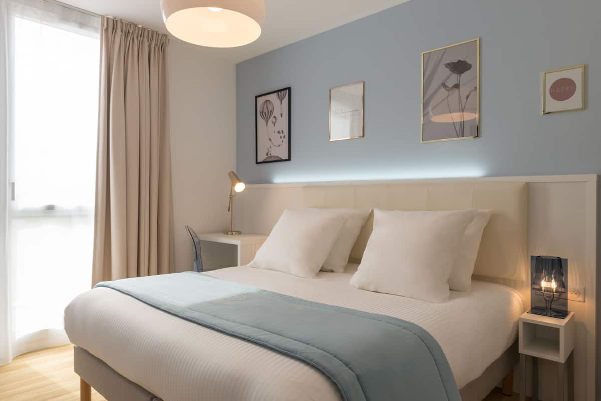 Een slaapkamer met een bed, nachtkastjes, een lamp en kunst aan de muur.