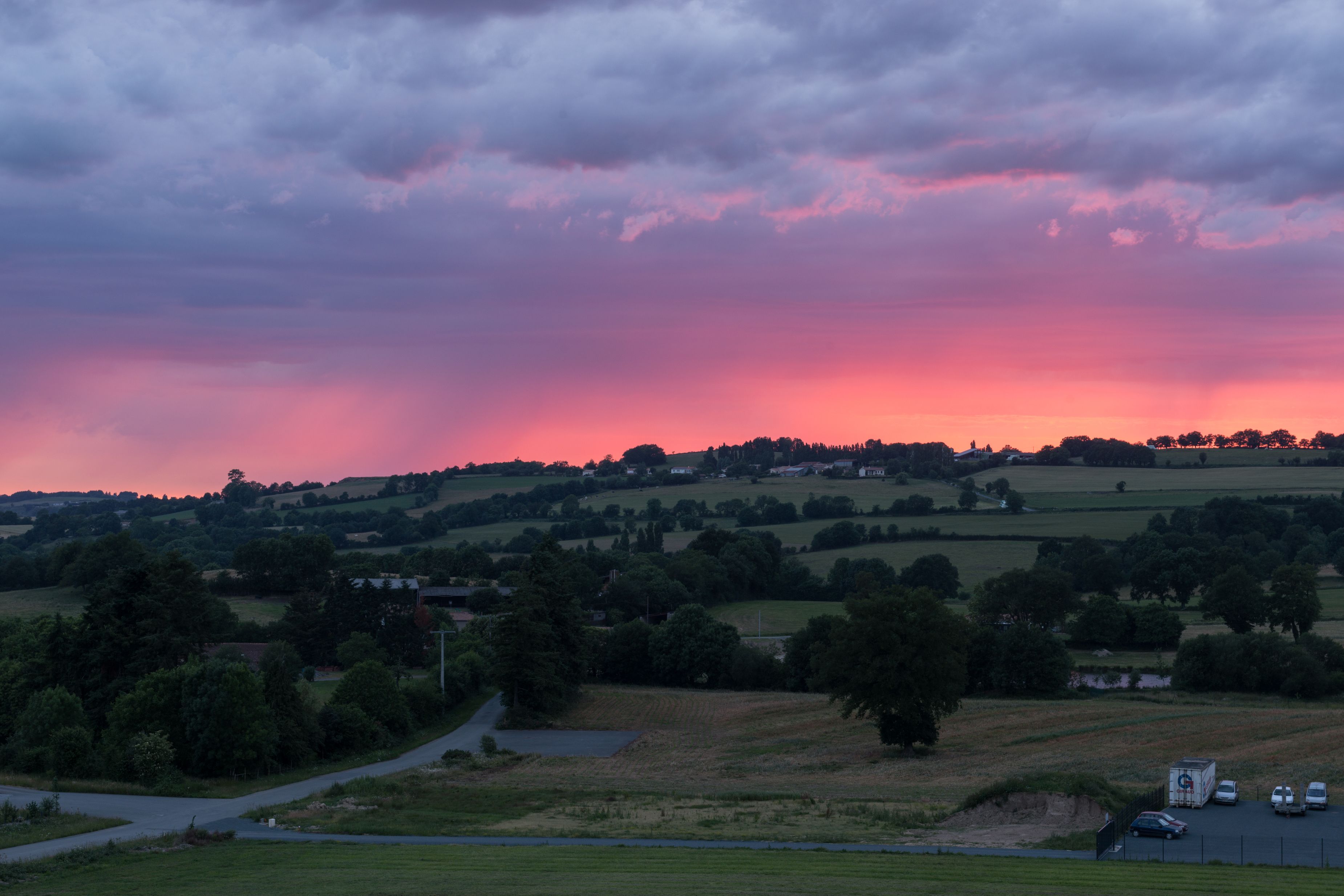 A rural landscape with rolling hills, a road, and a few vehicles.
