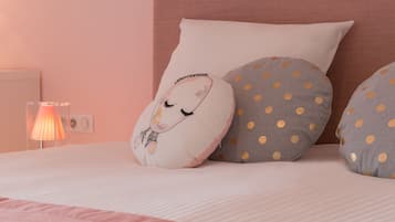 A bed with a pink blanket, a white pillow with a design, and two grey pillows with yellow polka dots.