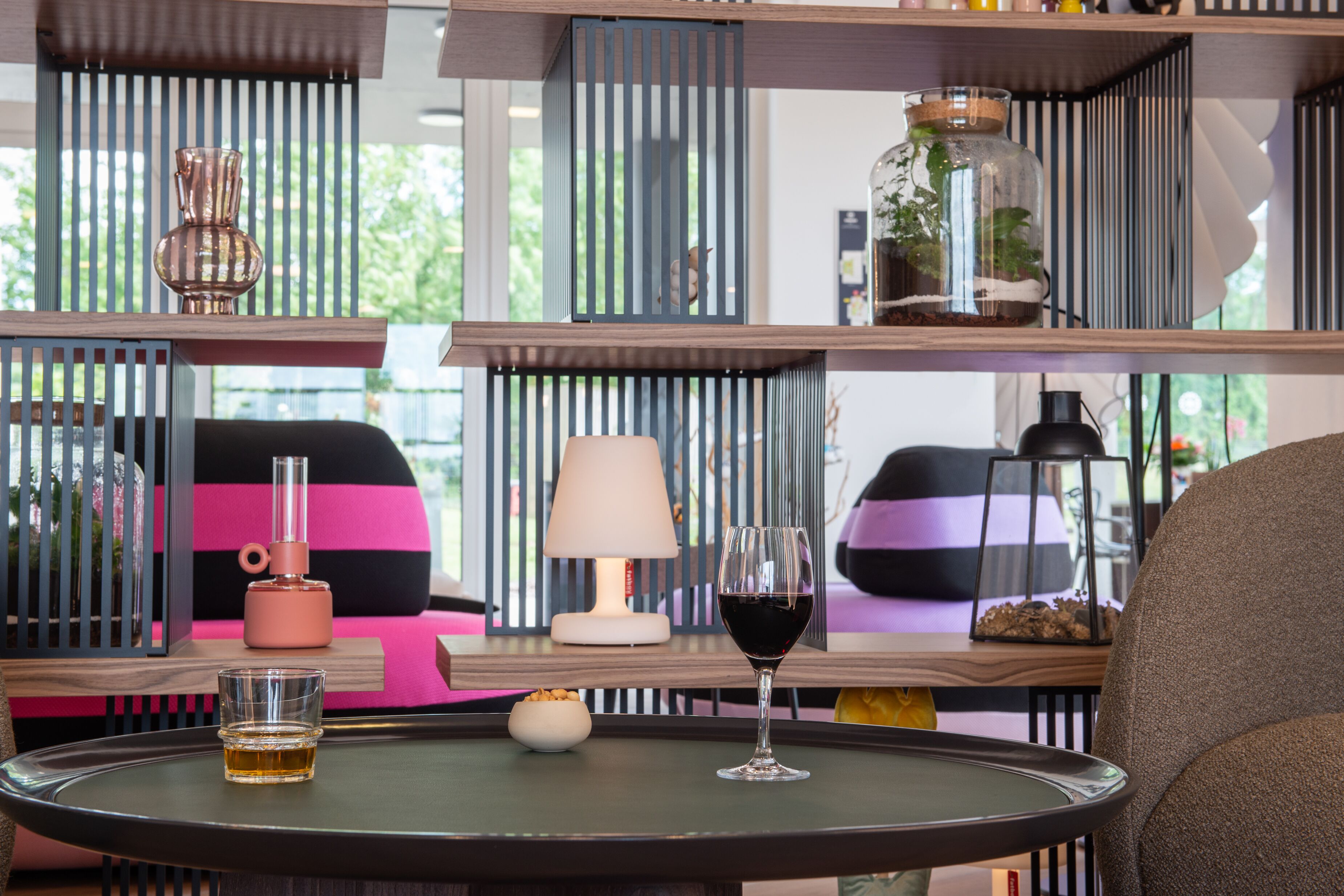 A modern living room with a glass table, a wine glass, a lamp, and a bookshelf.