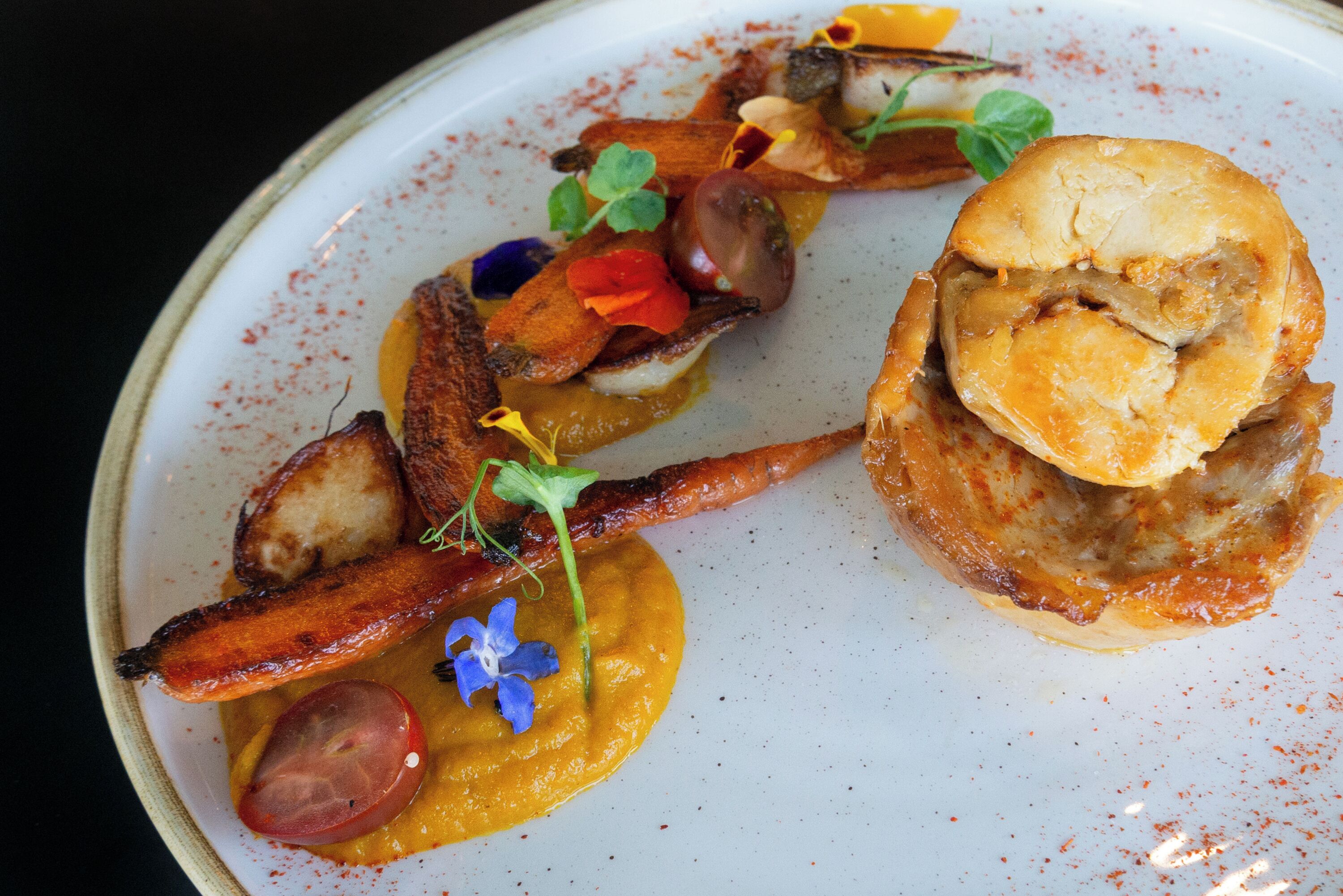 Un plato de comida con salchicha, un trozo de carne y un producto horneado, decorado con flores pequeñas.
