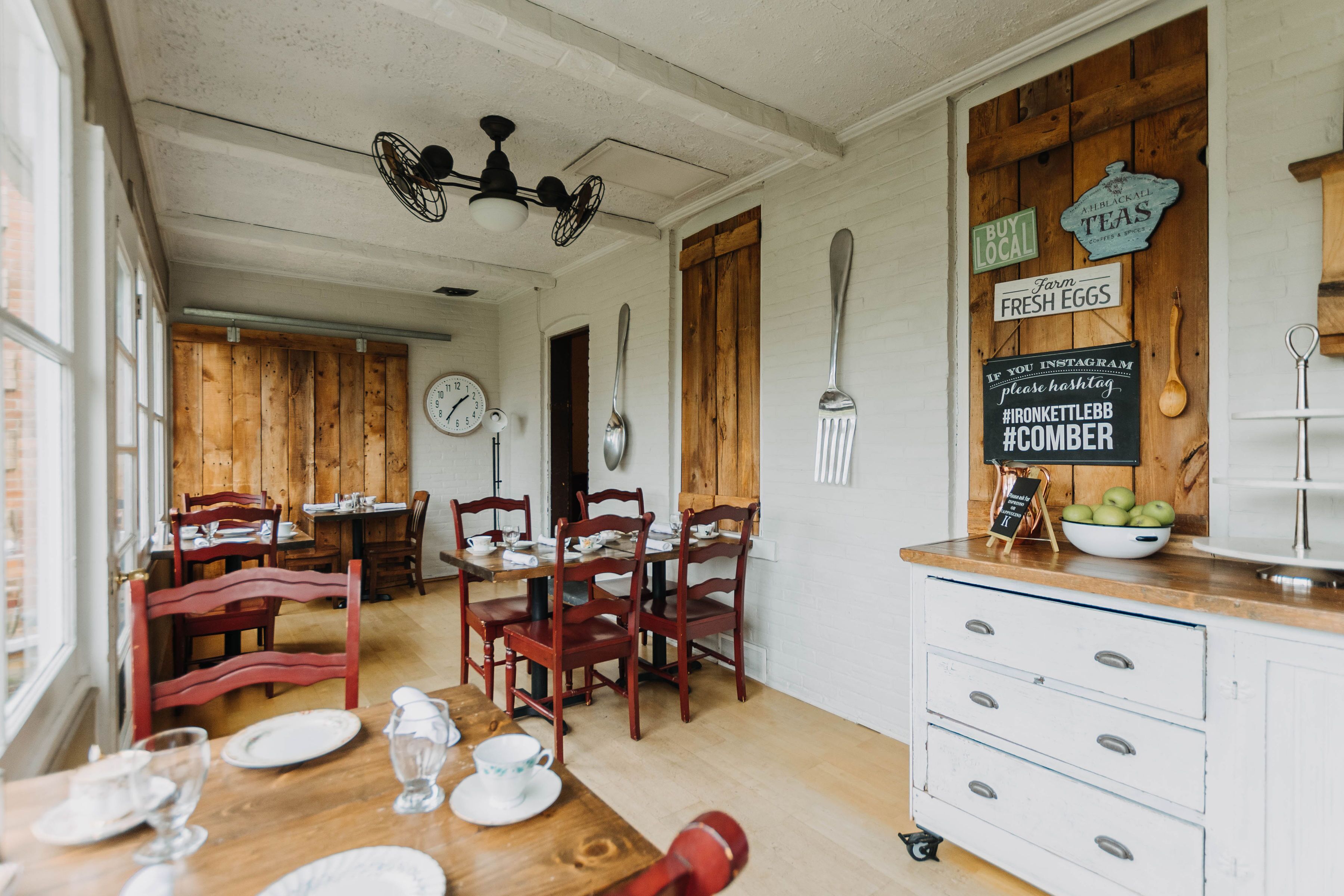 A dining area with wooden tables and chairs, a white cabinet with drawers, and a wall clock.