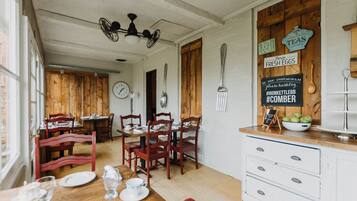 A dining area with wooden tables and chairs, a white cabinet with drawers, and a wall clock.