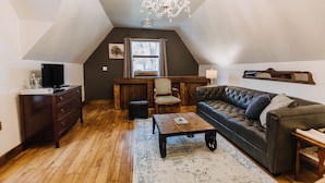 Een gezellige loft-achtige woonkamer met een donkerbruine leren bank, een houten salontafel en een kroonluchter.