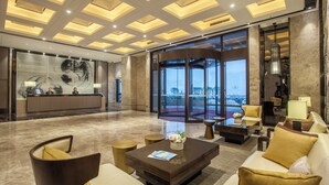 A spacious lobby with a reception desk, seating area, and large windows offering a view of the outdoors.