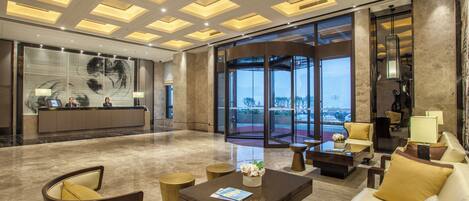 A spacious lobby with a reception desk, seating area, and large windows offering a view of the outdoors.