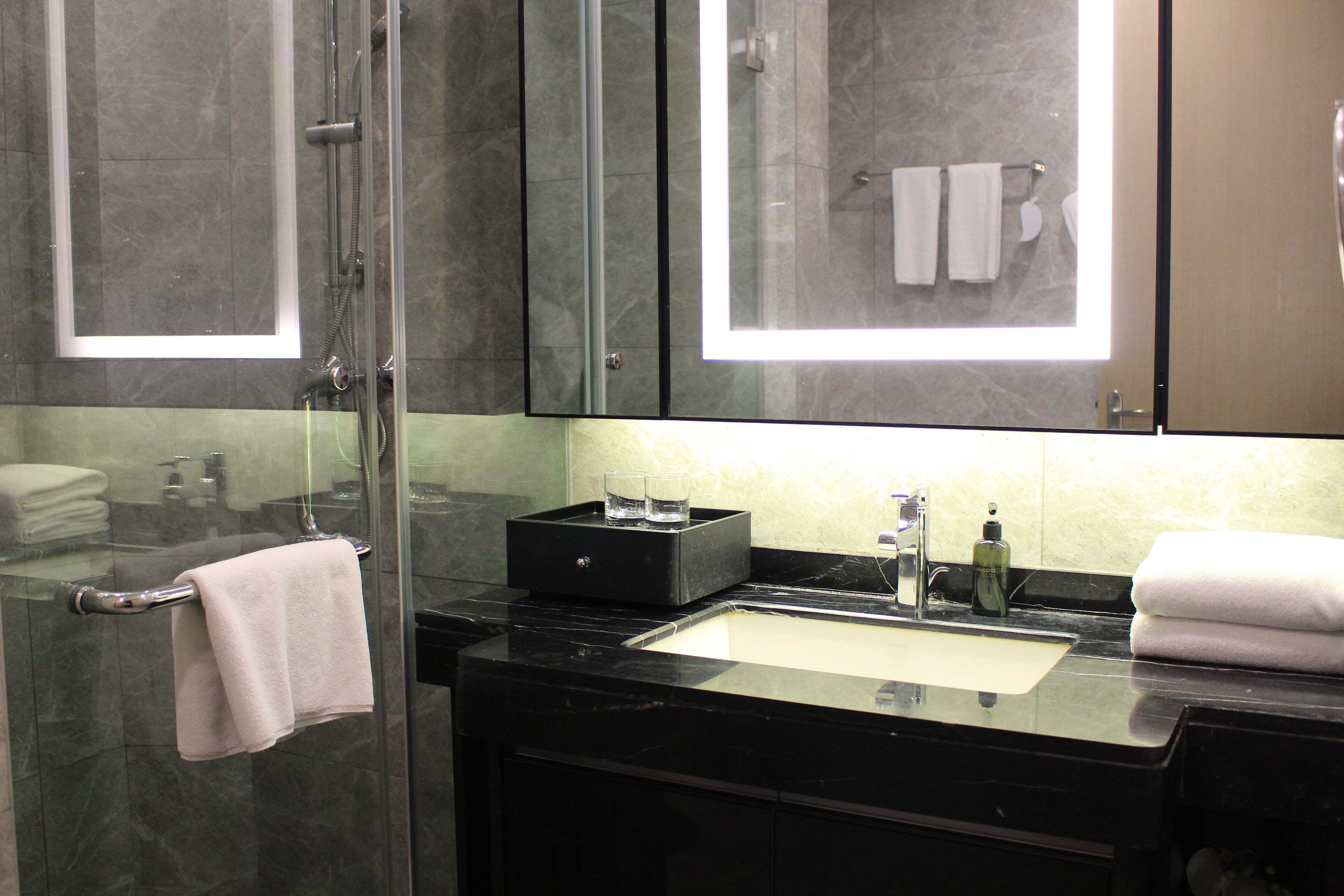 A modern bathroom with a glass-enclosed shower, a black marble sink, and a large mirror above the vanity.