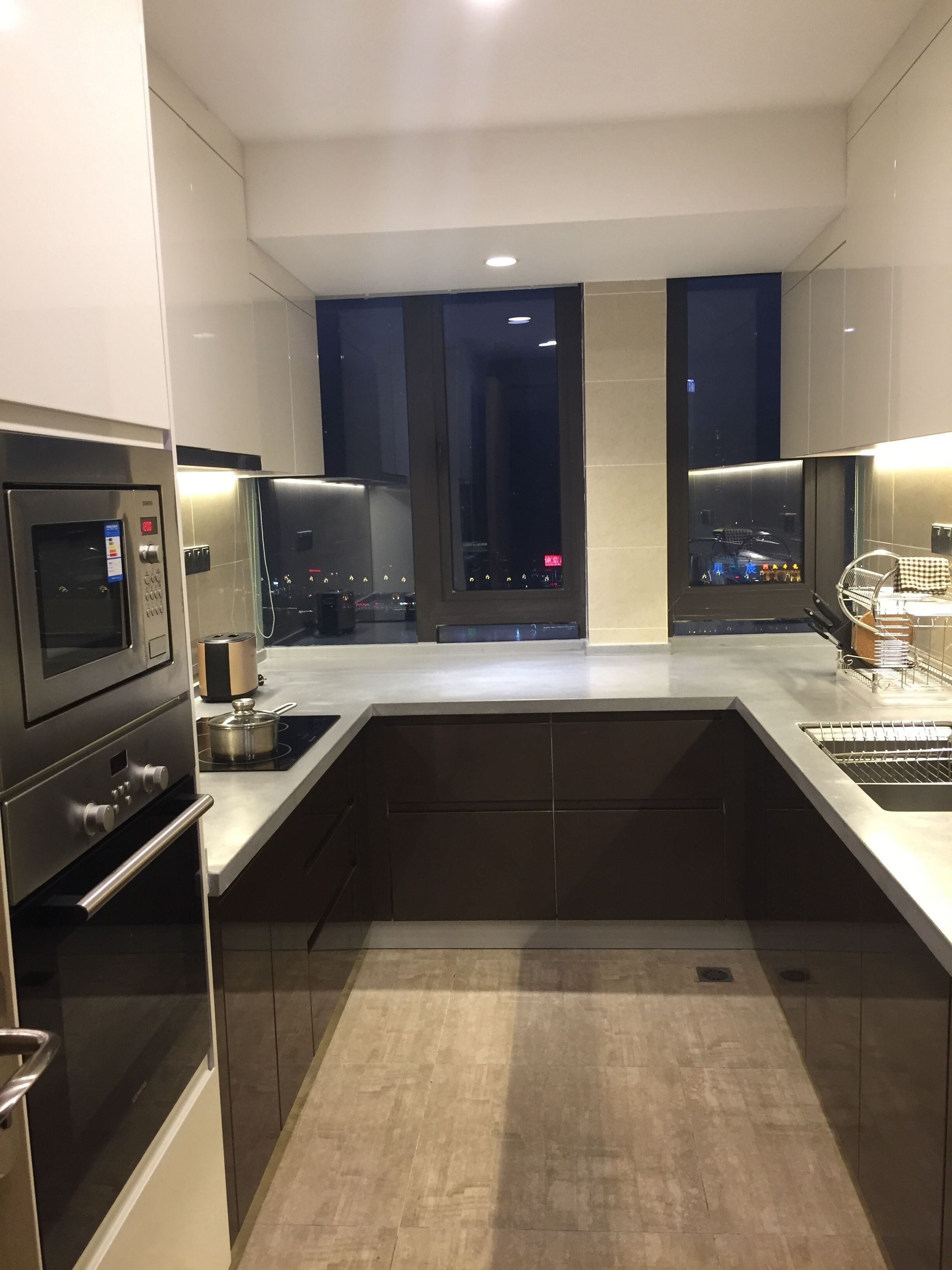 A modern kitchen with a built-in oven, microwave, and stove. There is a large window with a view of the city at night.