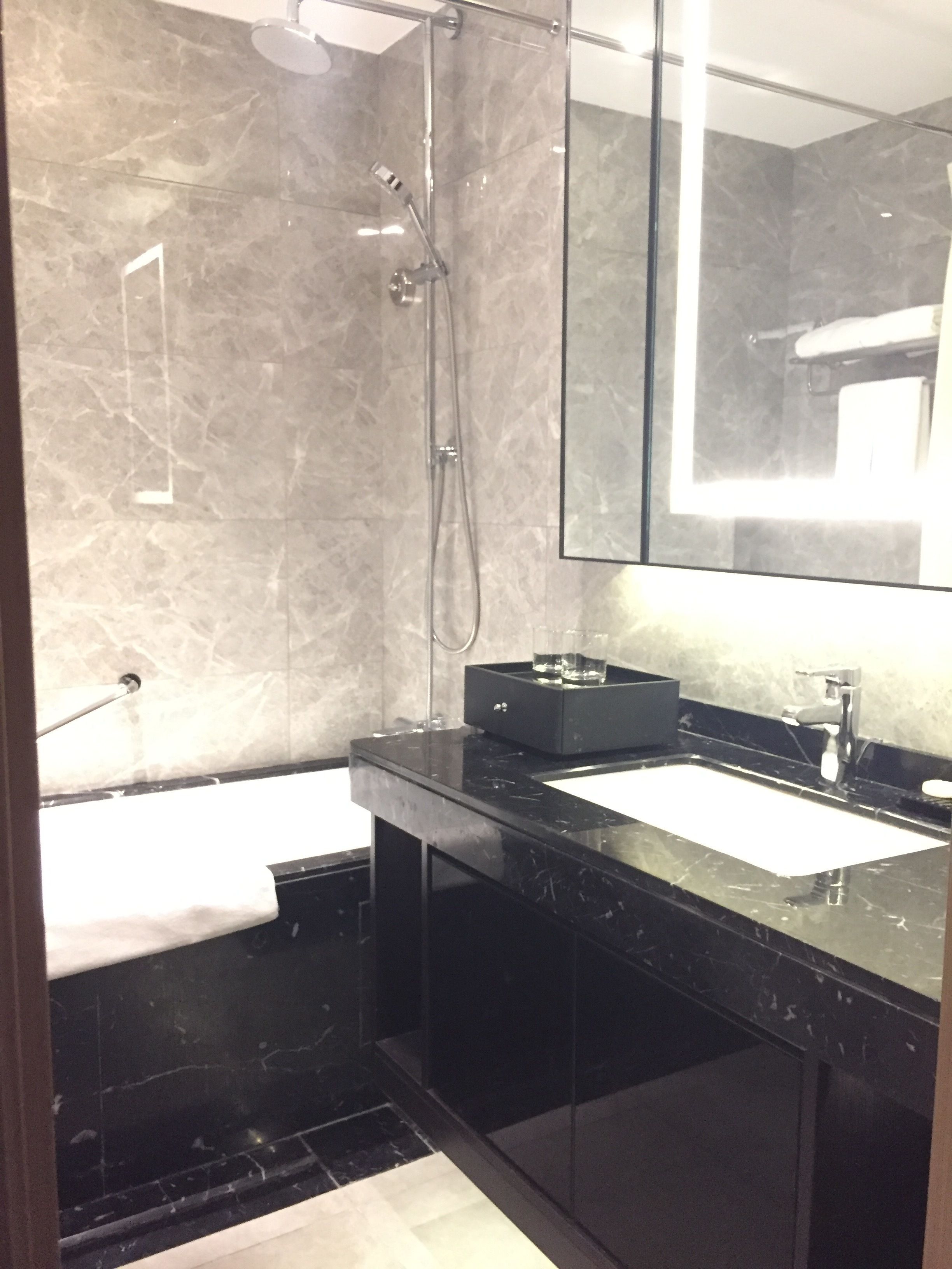 A modern bathroom with a glass shower enclosure, a black countertop, and a large mirror.