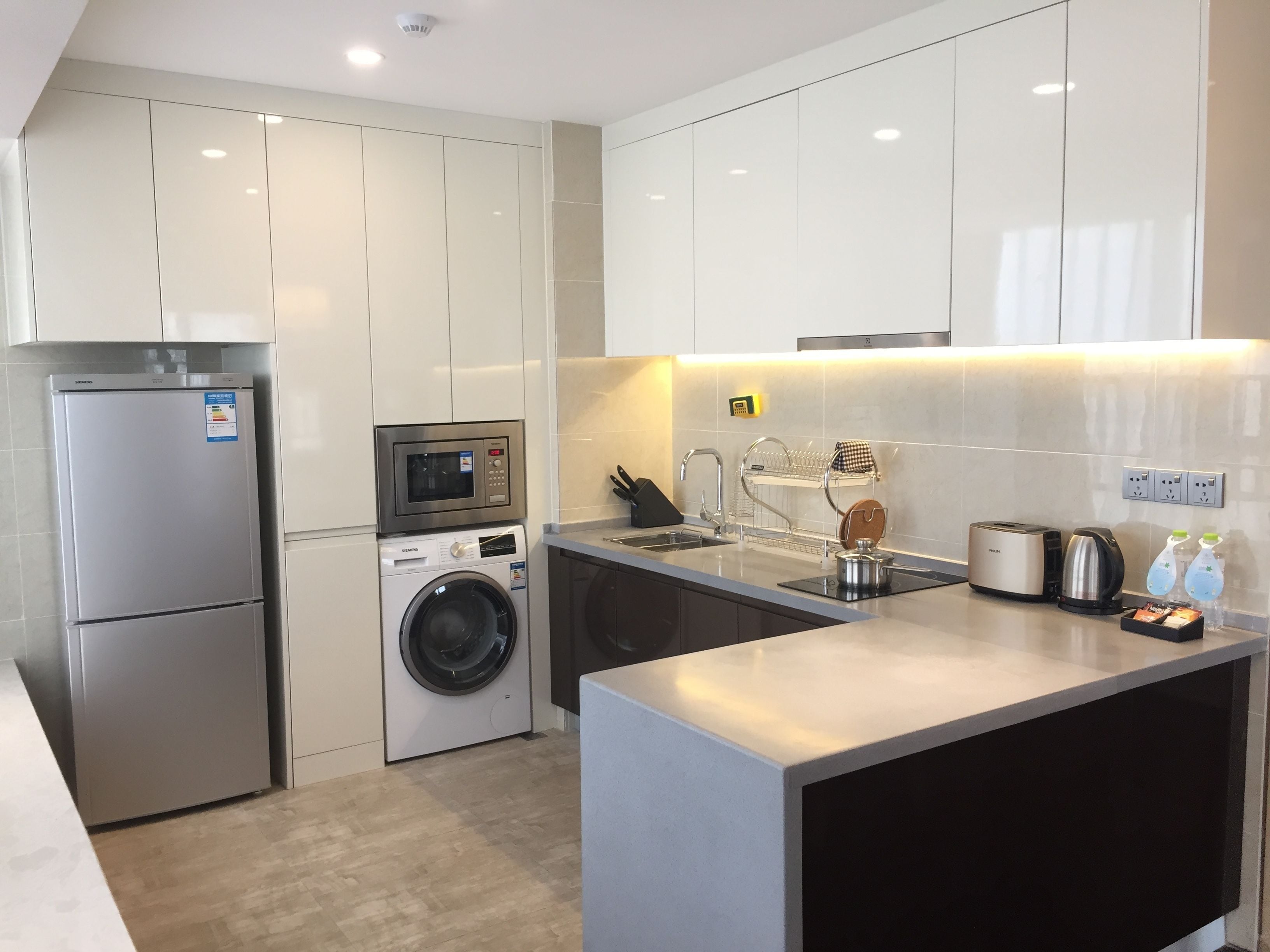 A modern kitchen with stainless steel appliances, a built-in washing machine, and a compact island with a kettle and toaster.
