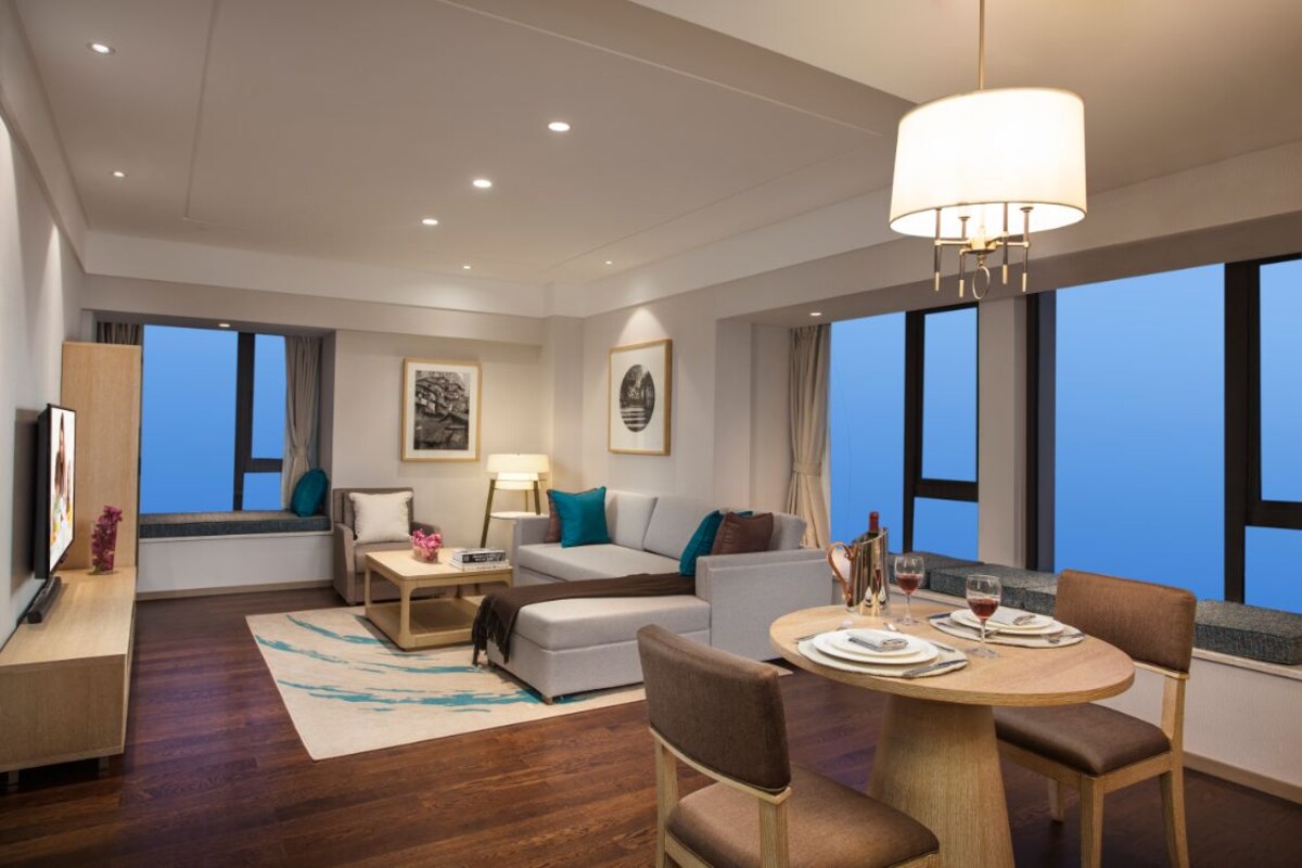 Una habitación de hotel moderna con sofá, una mesa de comedor para dos personas, televisión y obras de arte en las paredes.