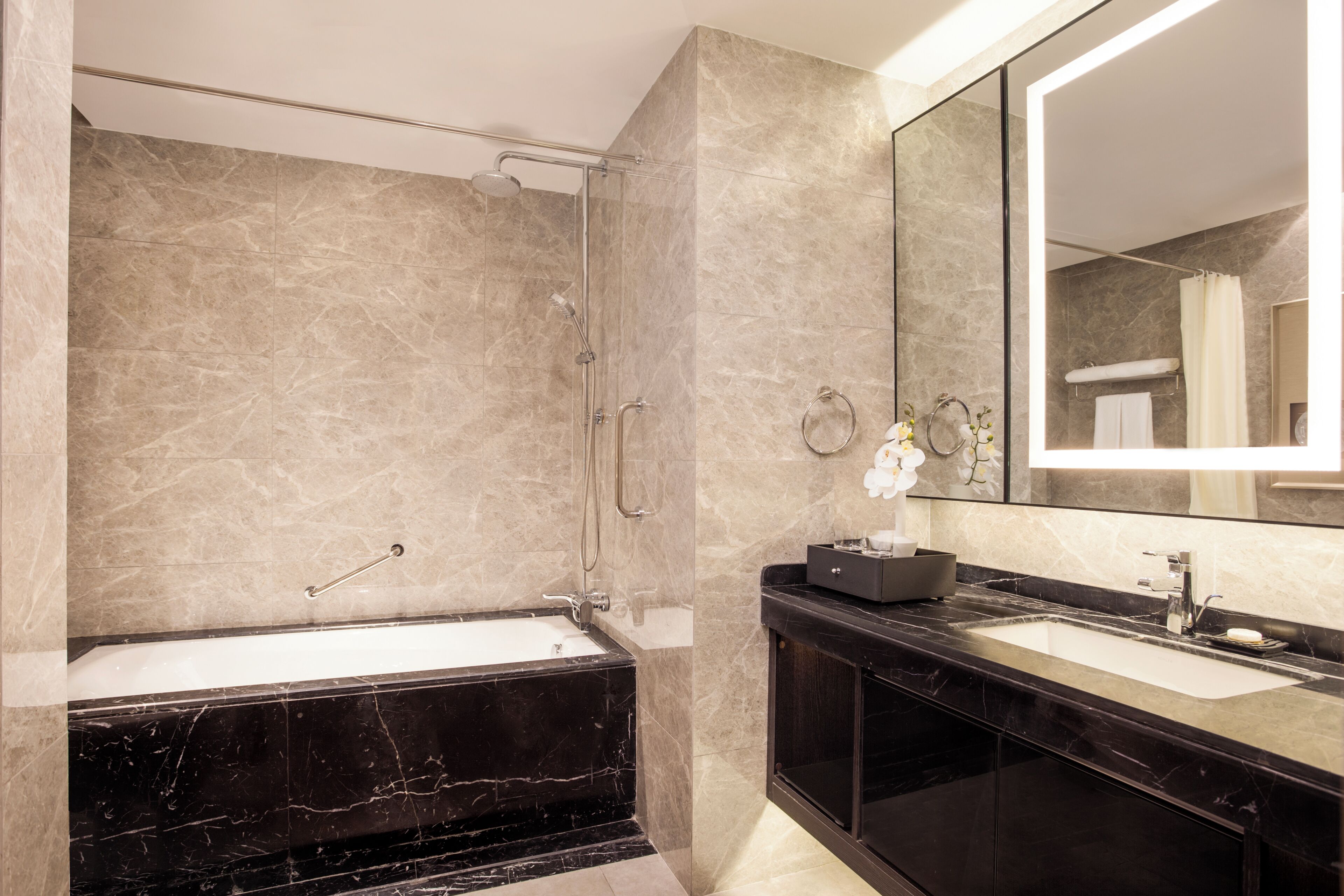 A modern bathroom with a marble shower, a black bathtub, and a large mirror above the sink.