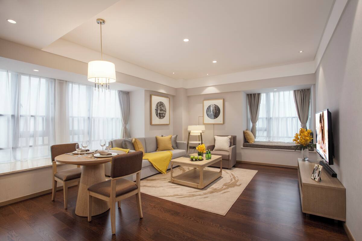 A modern hotel room with a dining area, a sofa set, a coffee table, and a television.