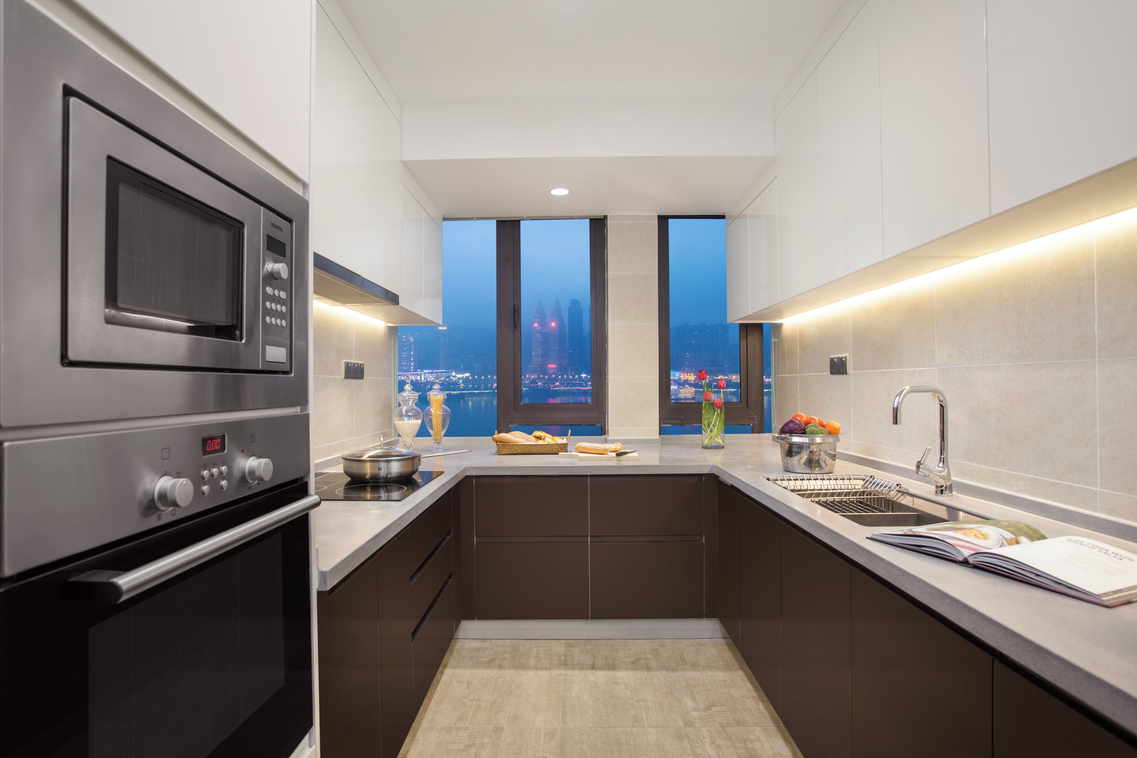 A modern kitchen with a built-in oven, microwave, and sink. It features large windows with a city view.