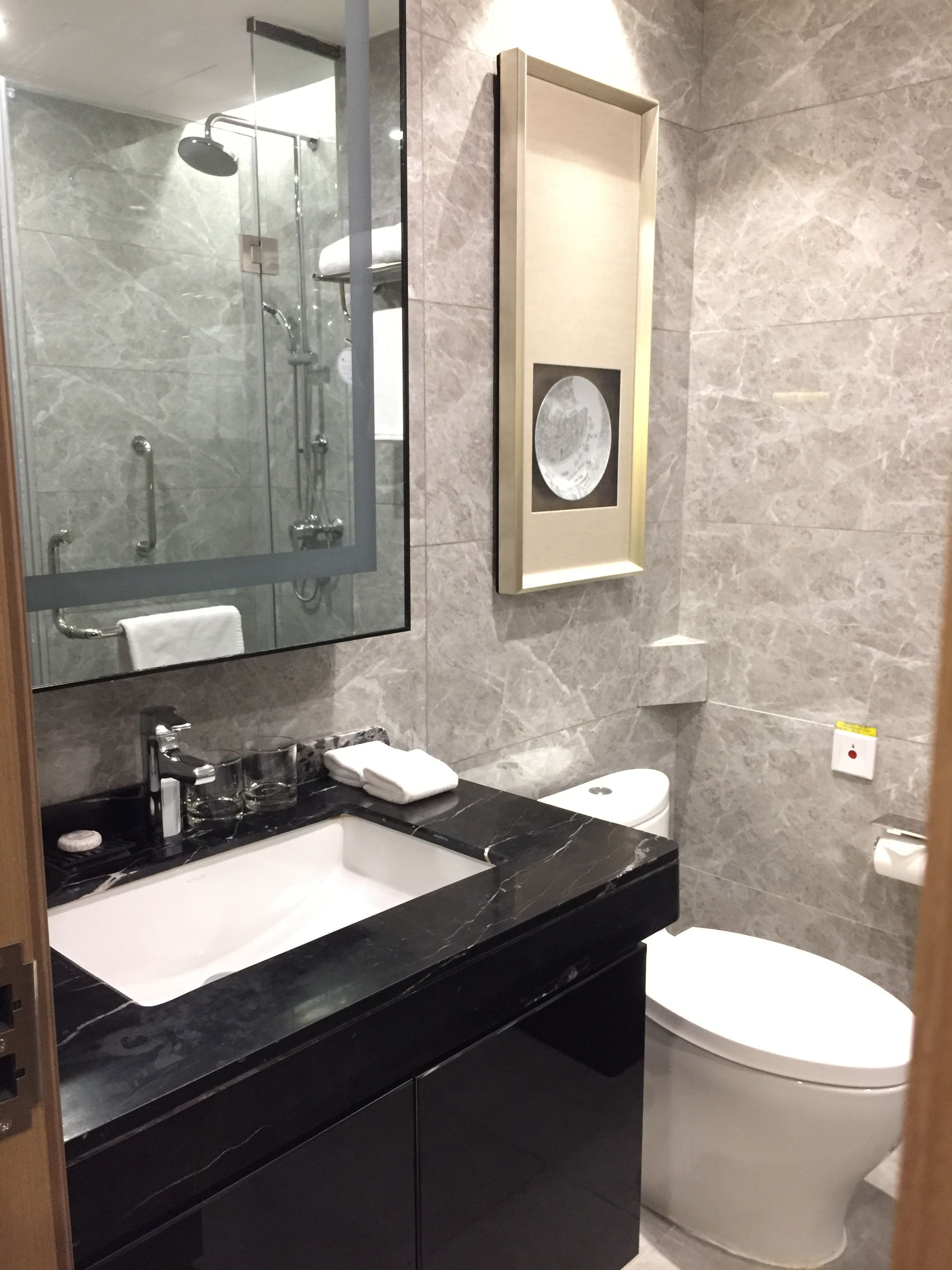 A modern bathroom with a glass-enclosed shower, a white toilet, and a black marble sink.