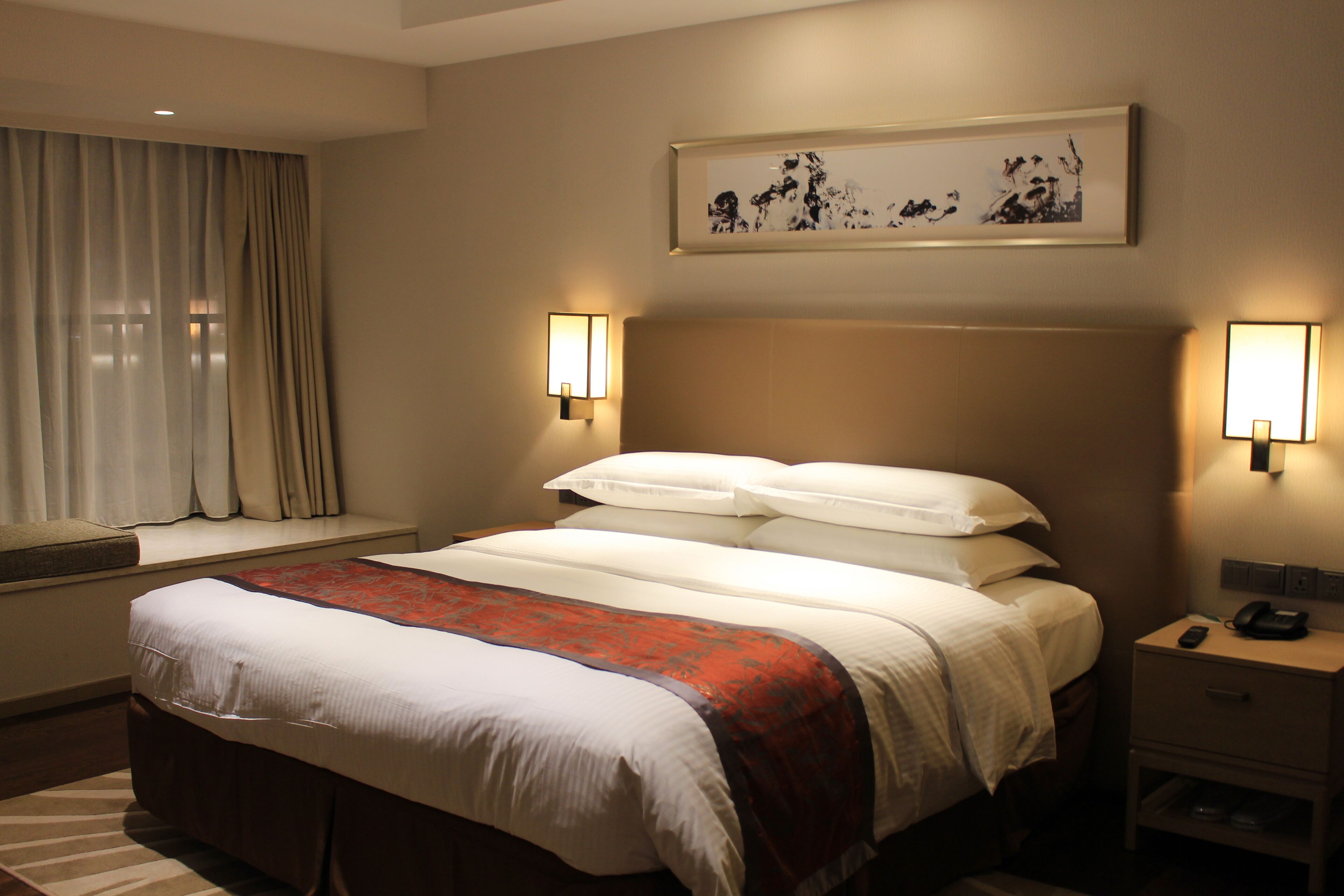 Une chambre d’hôtel avec un grand lit, des lampes de chevet, une fenêtre avec des rideaux et un tableau au mur.