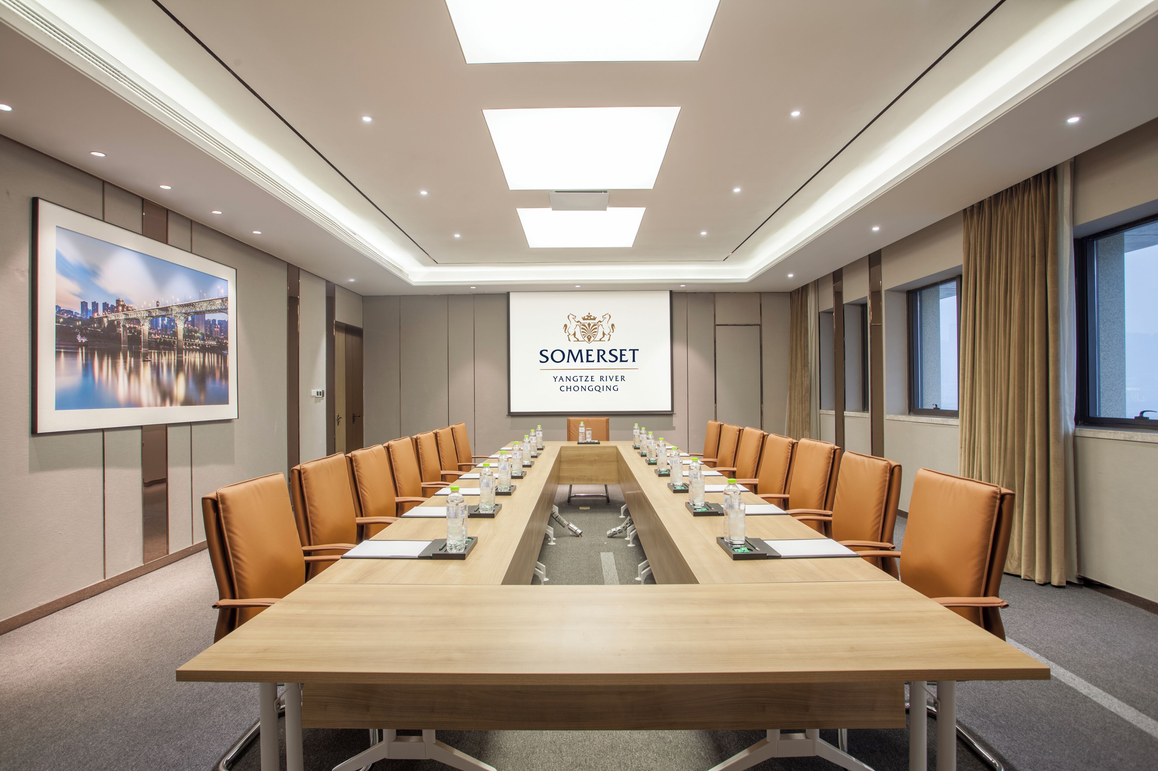 A conference room with a long table, chairs, a projector screen, and a framed picture on the wall.