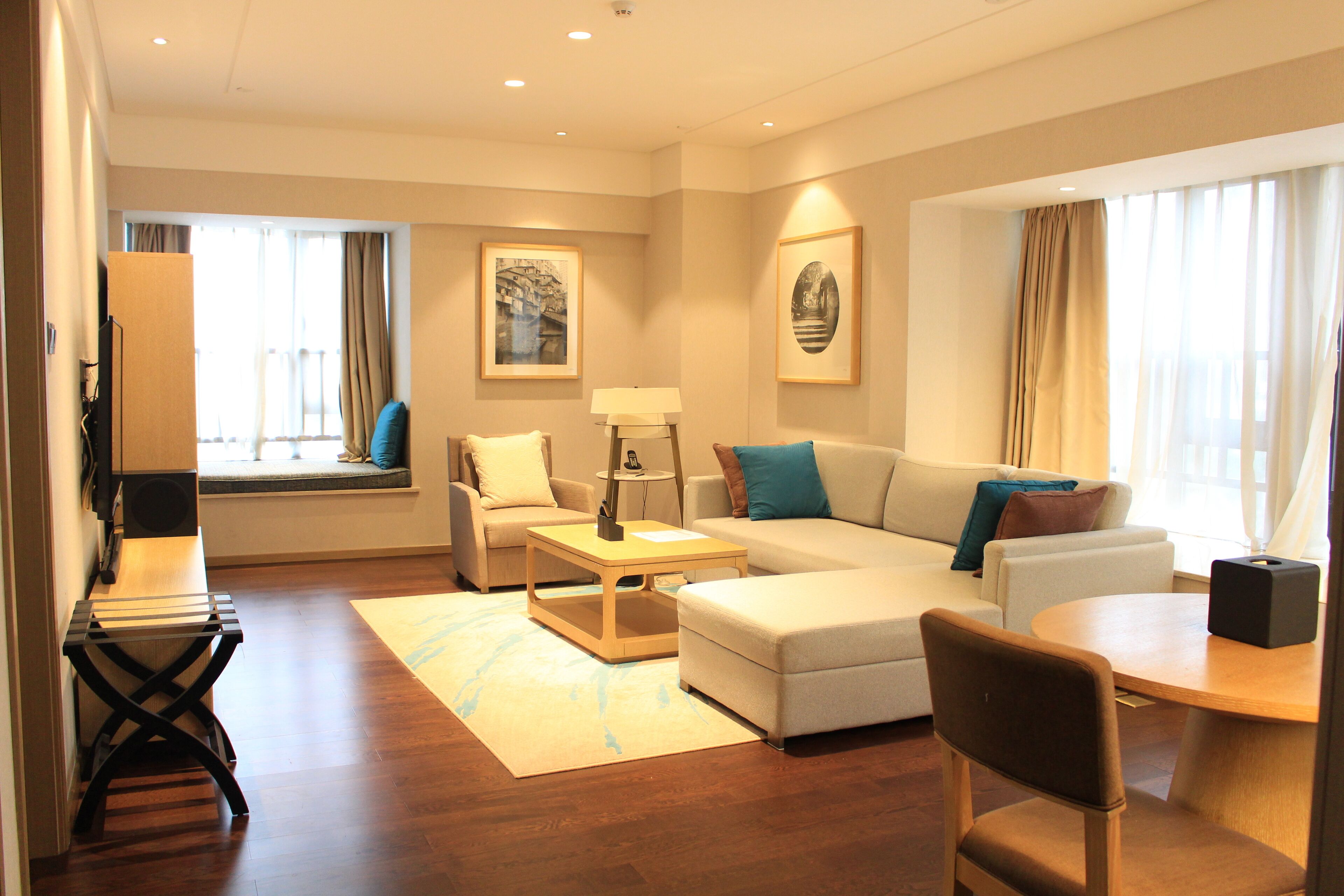 A modern hotel room with a sofa, armchair, coffee table, and a small dining table.
