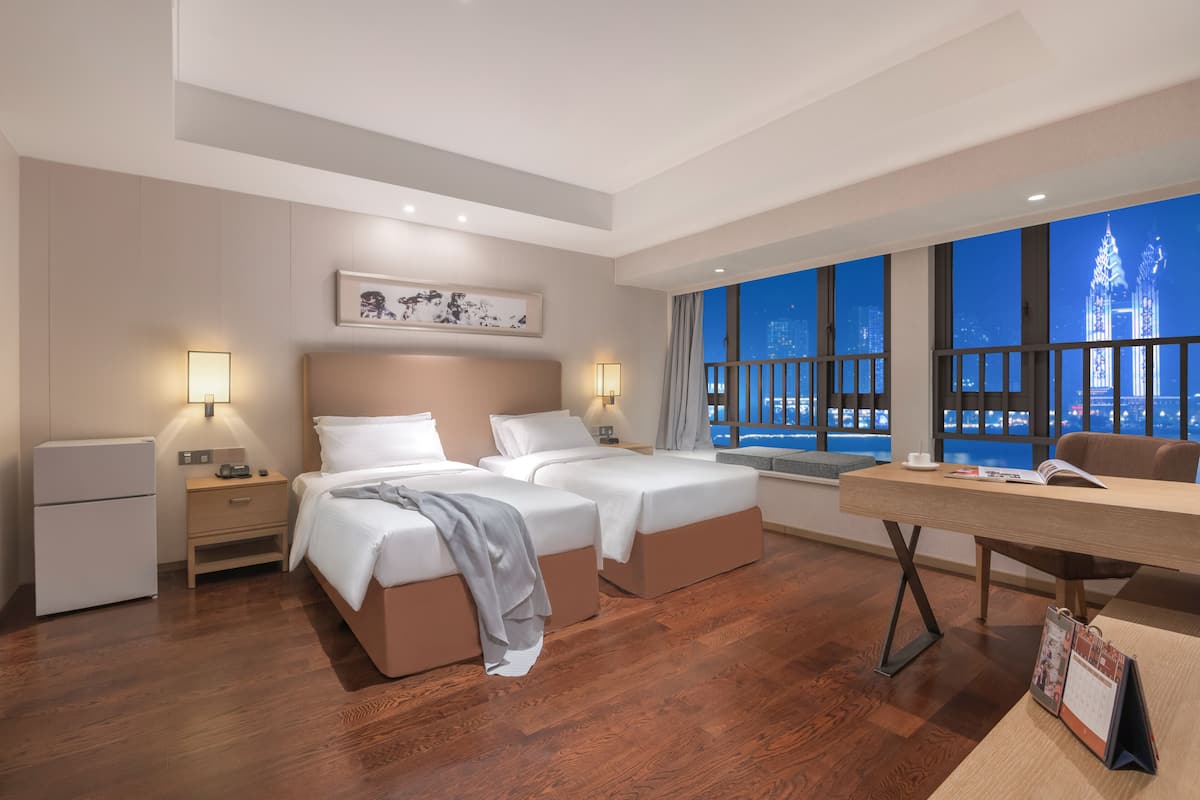 A hotel room with two beds, a desk, and a view of a cityscape at night.