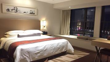 Une chambre d’hôtel avec un grand lit, un bureau, une fenêtre donnant sur la ville et une œuvre d’art encadrée au mur.