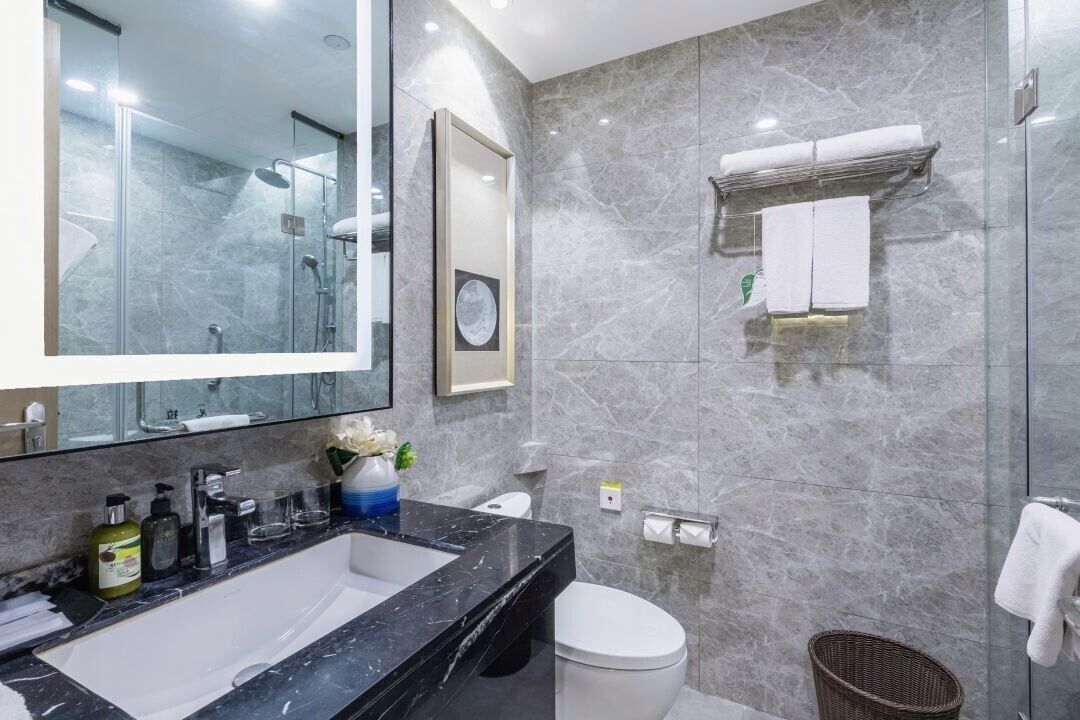 Un bagno moderno con un ampio specchio, un lavabo in marmo nero, un WC e uno spazio doccia in vetro.
