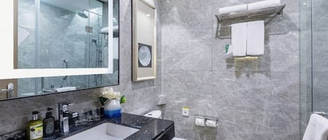 A modern bathroom with a large mirror, a black marble sink, a toilet, and a glass shower enclosure.