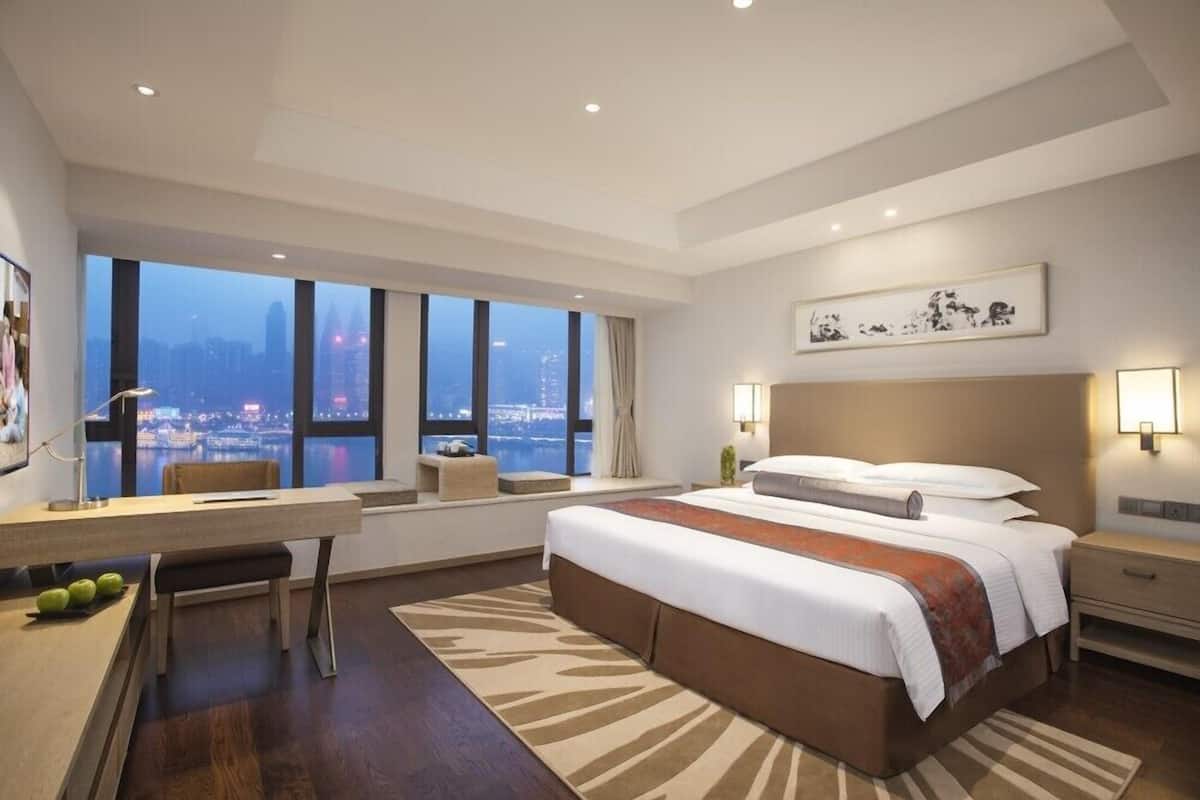 A modern hotel room with a large bed, a desk, and a view of the cityscape.