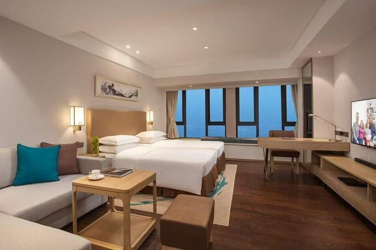 A modern hotel room with a large bed, a sofa, a desk, and a TV.