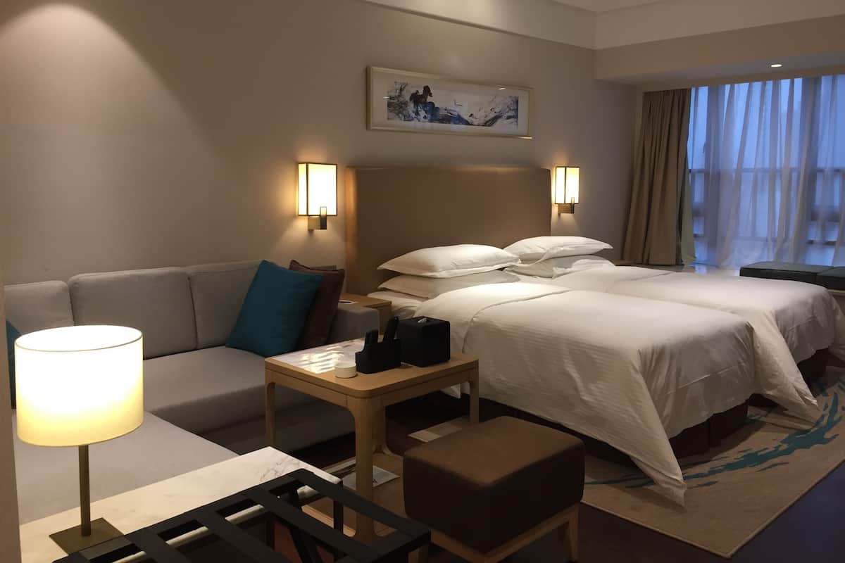 A hotel room with a bed, a sofa, a small table, and a lamp.