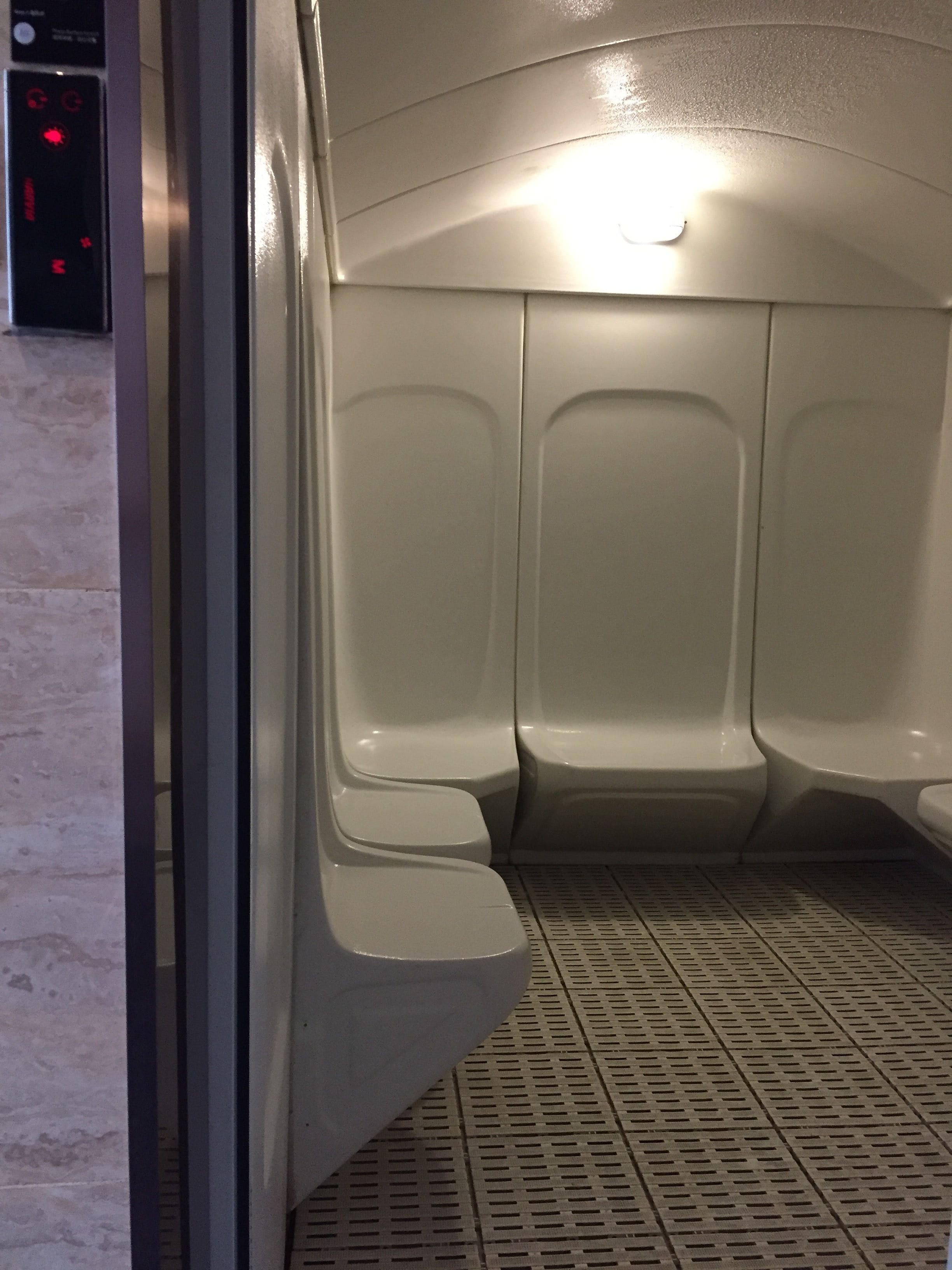 A restroom with three toilets, a control panel, and a tiled floor.