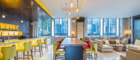 A modern hotel lobby with a long bar, seating area, and large windows offering city views.