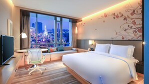 A hotel room with a large bed, a desk with a computer, a chair, and a view of a cityscape at night. - Hilton Garden Inn Ningbo (Ningbo)