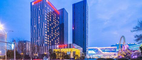 Un hotel moderno con un letrero rojo llamativo, rodeado de edificios altos y una calle bien iluminada.