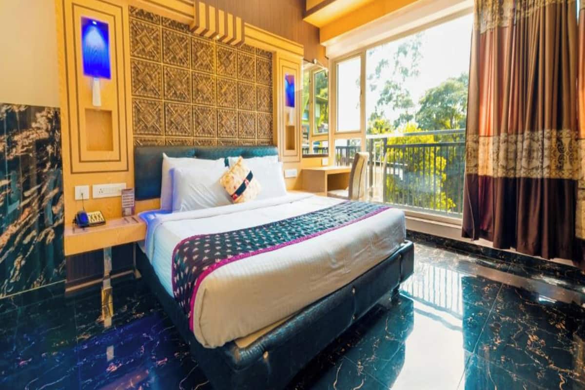 A spacious hotel room with a large bed, a desk, and a balcony with curtains.
