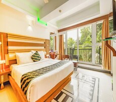Ein Hotelzimmer mit einem großen Bett, einem Schreibtisch, einem Sessel und einem Balkon mit Blick ins Grüne.