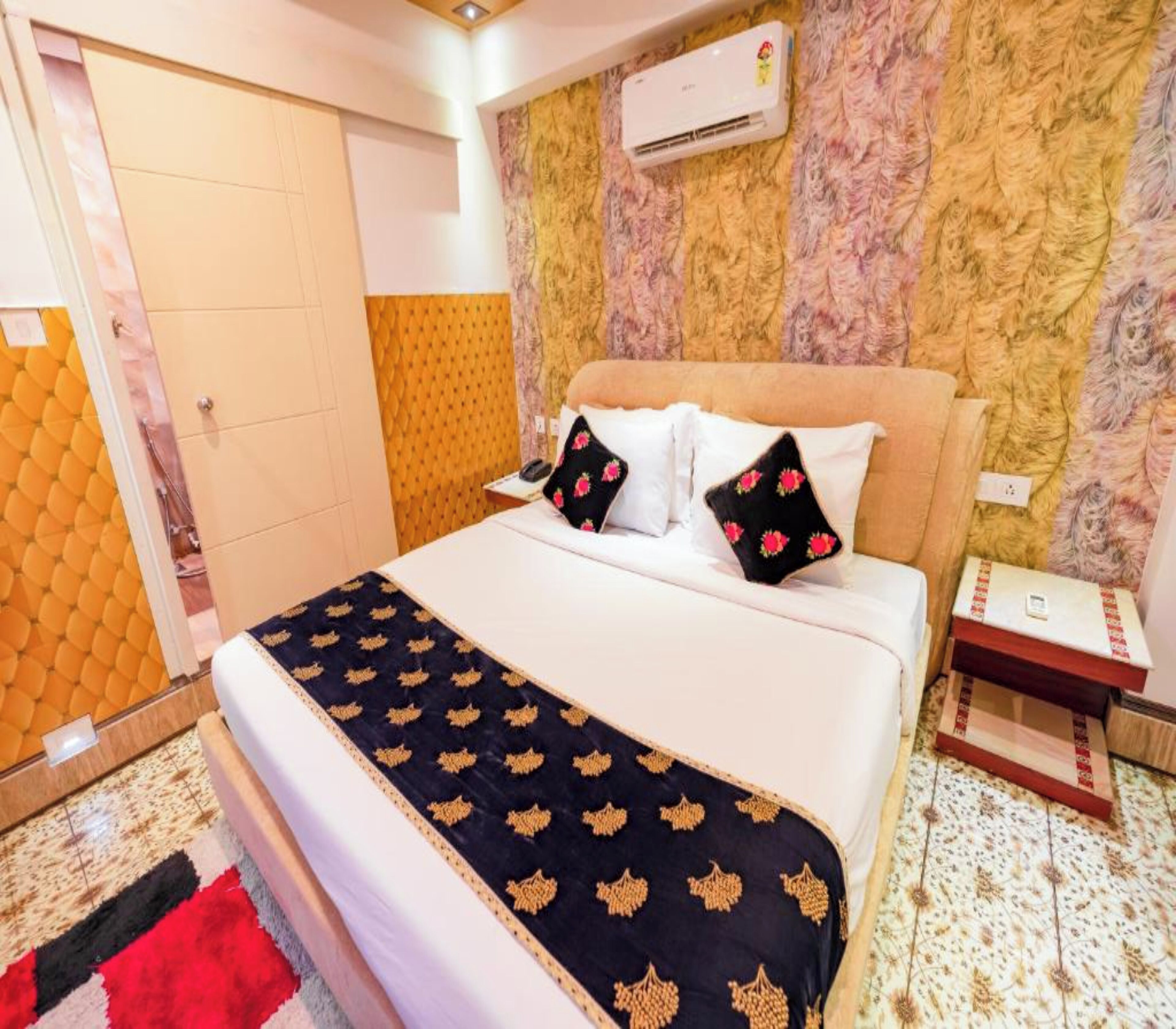 A hotel room with a bed, a nightstand, an air conditioning unit, and a patterned wall.