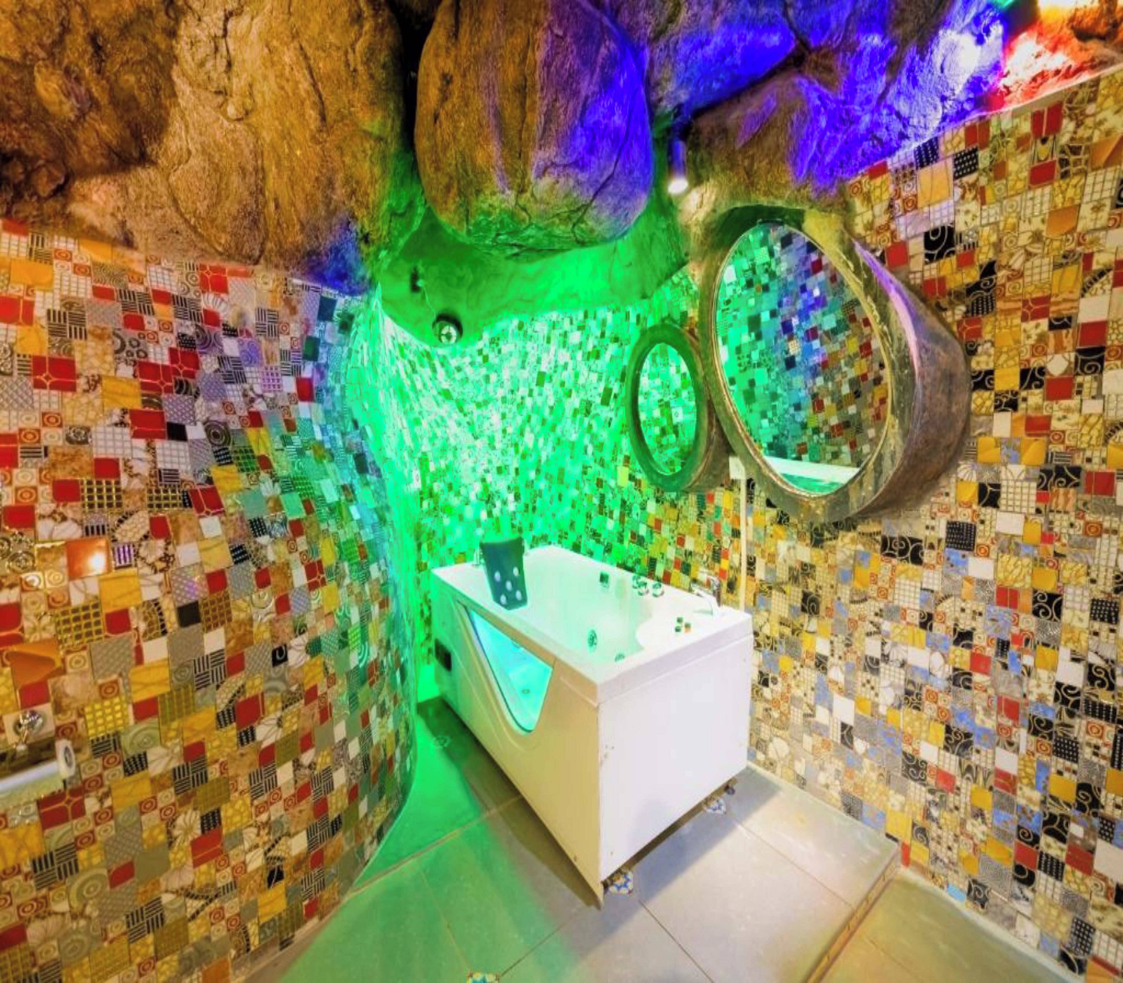 A bathroom with a mosaic wall, a white bathtub, and a green light.