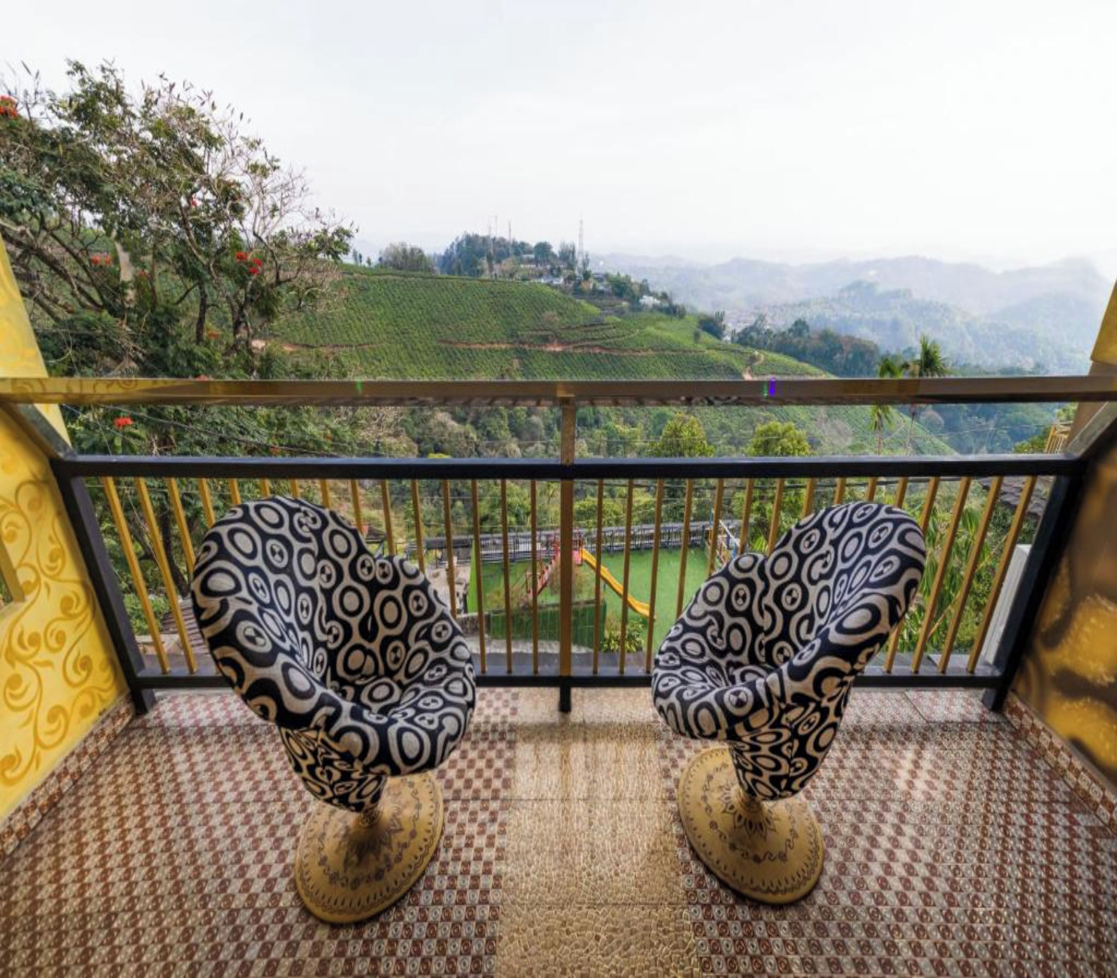 Deux chaises à motifs sur un balcon, avec vue sur des collines verdoyantes et une chaîne de montagnes lointaine.