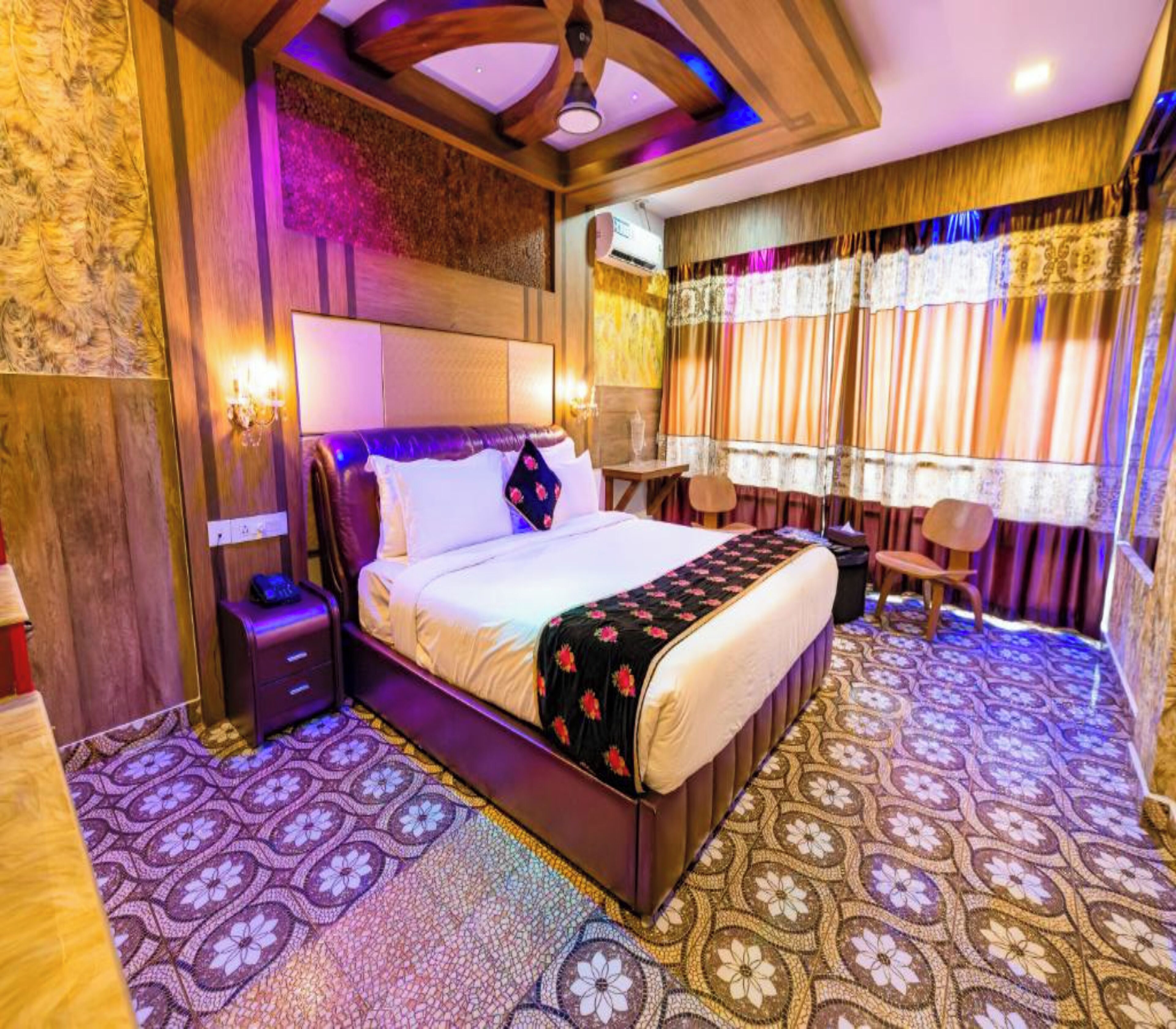 A hotel room with a large bed, a wooden headboard, a small table, and a chair.