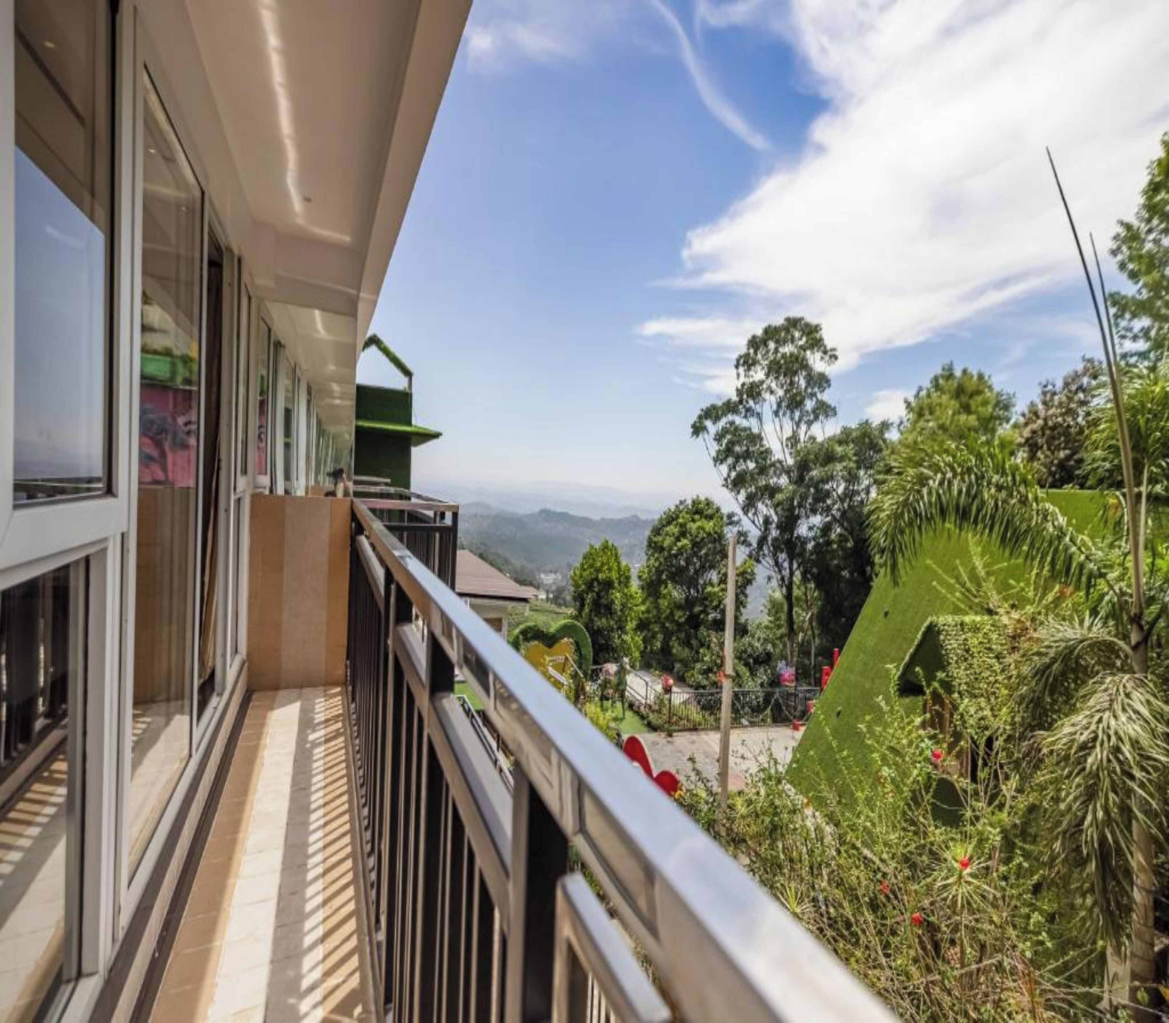 A balcony with a view of a lush garden and distant mountains.