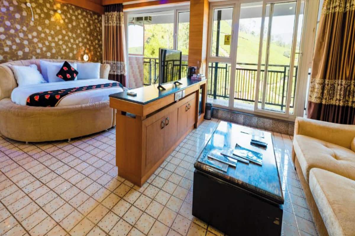 A spacious living area with a sofa, a coffee table, and a TV on a wooden cabinet. Large windows offer a view of the outdoors.