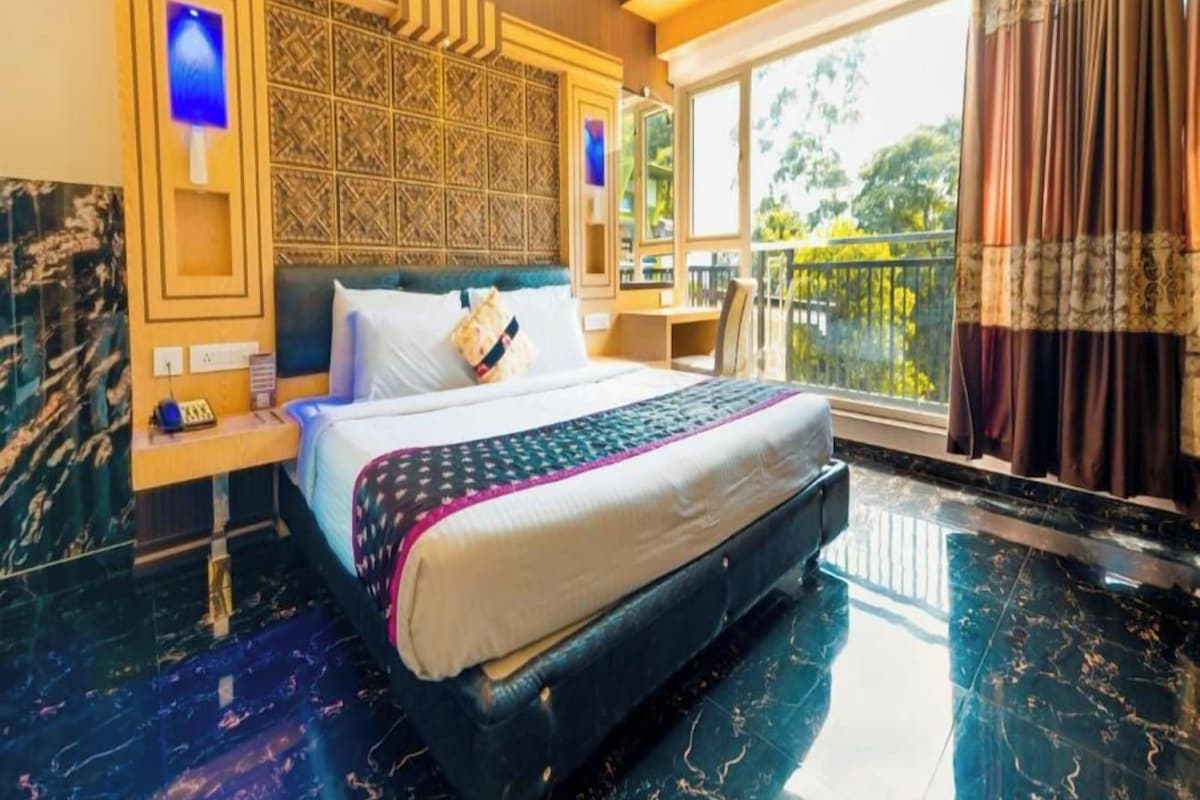 A hotel room with a bed, a nightstand, a window with curtains, and a balcony.