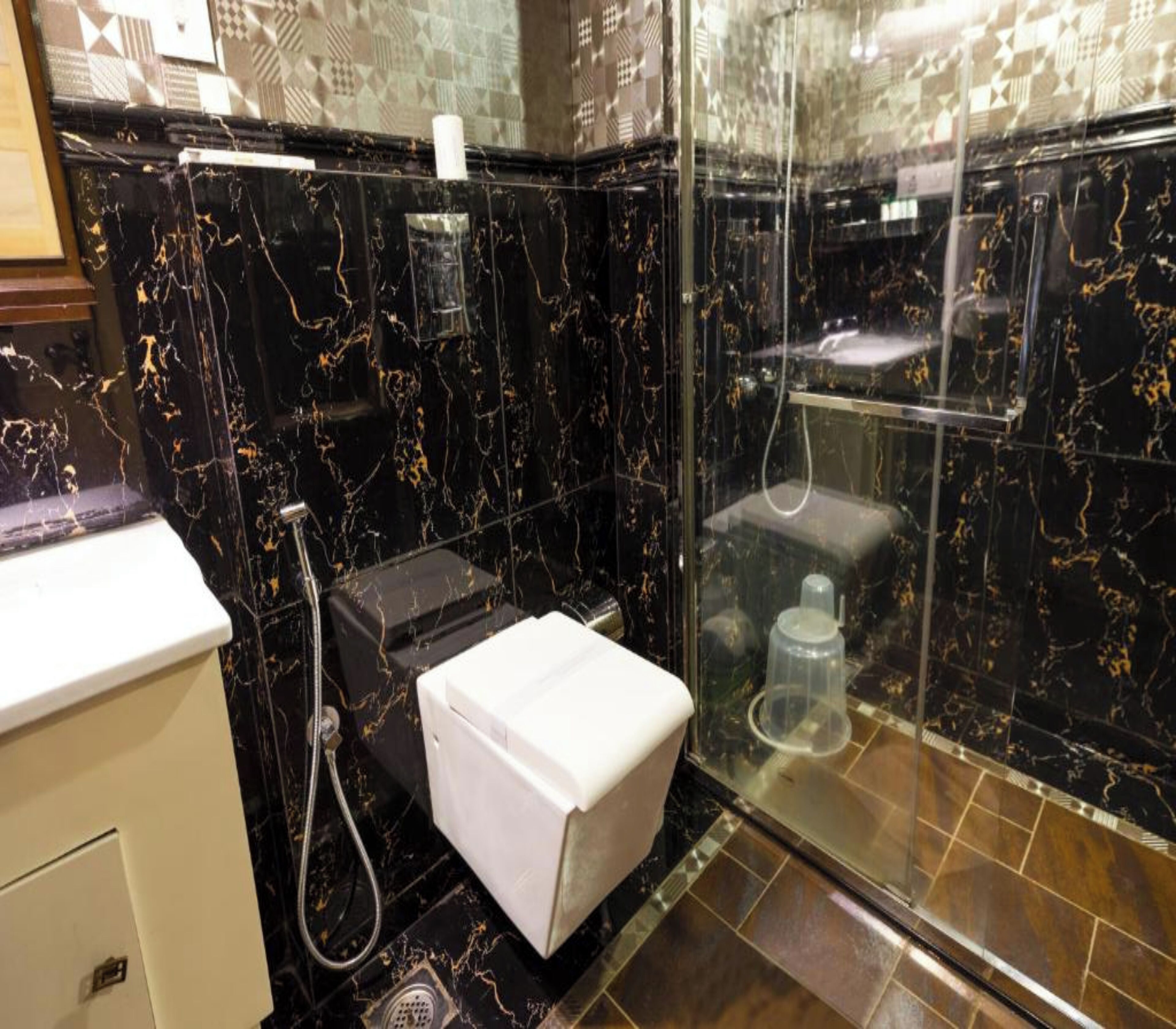 A modern bathroom with a black marble wall, a white sink, and a glass-enclosed shower area.