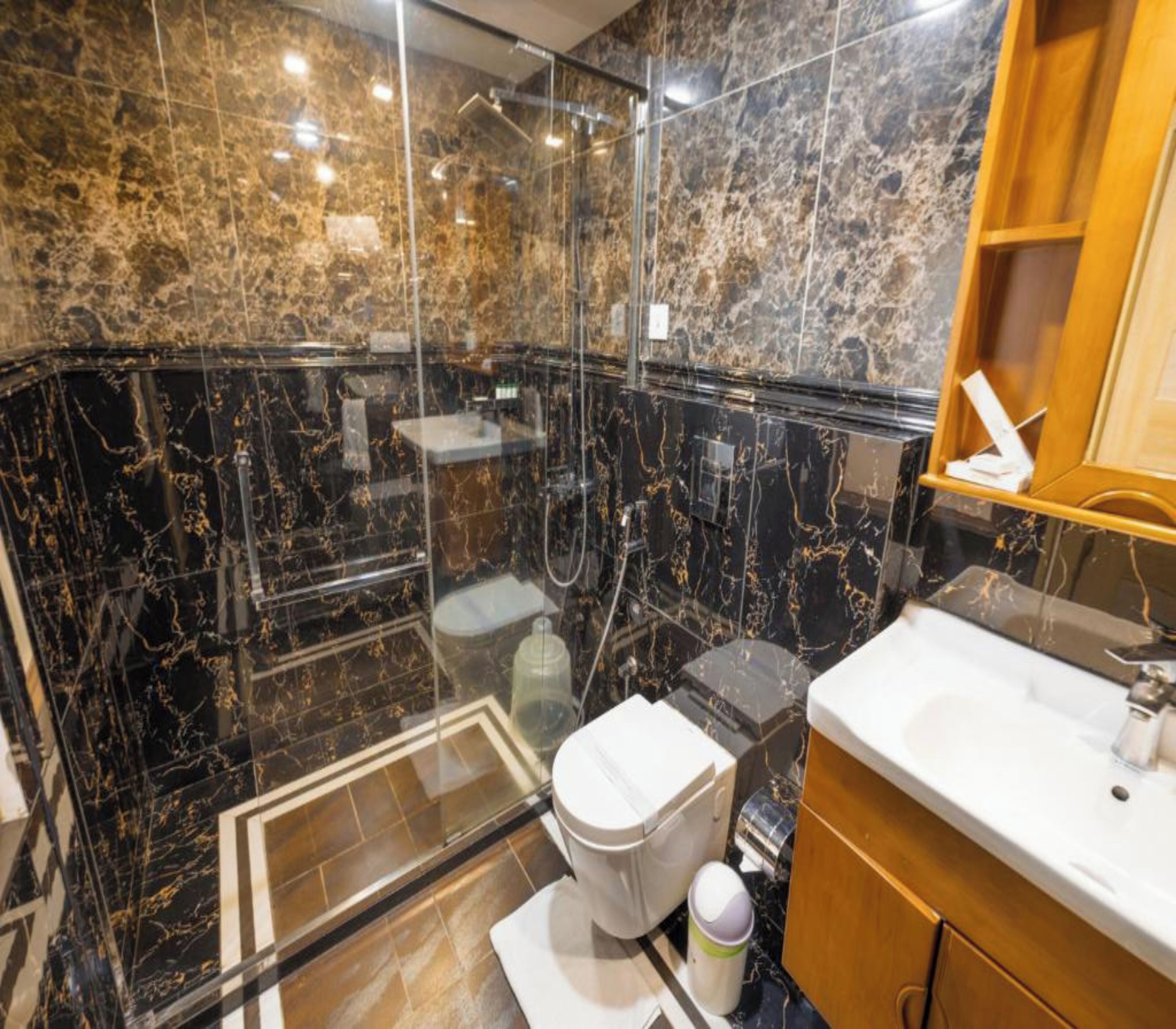 A modern bathroom with a glass-enclosed shower, a white toilet, and a wooden vanity with a sink.