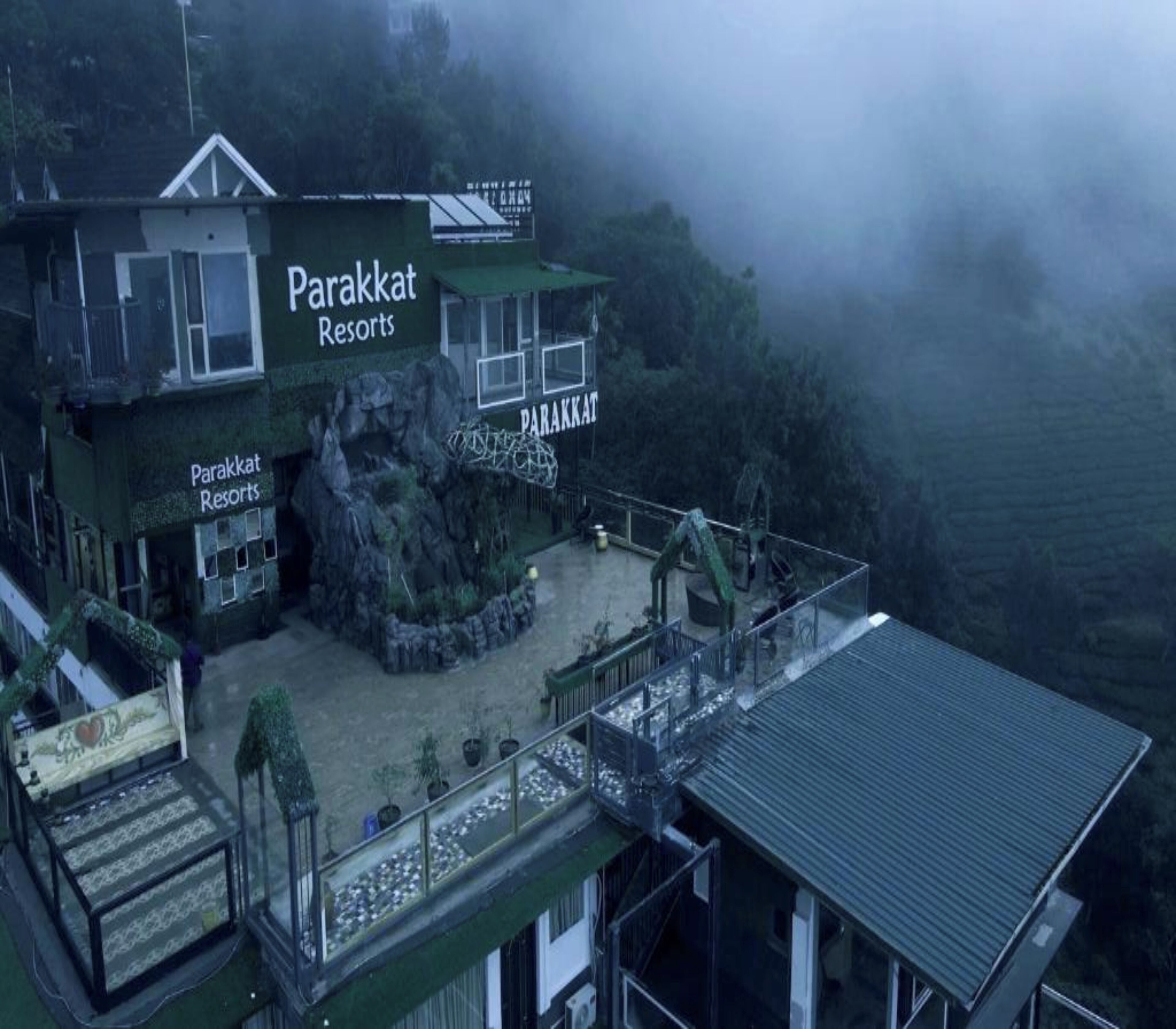 A Parakkat Resort building with a rocky facade, a balcony, and a view of the surrounding landscape.