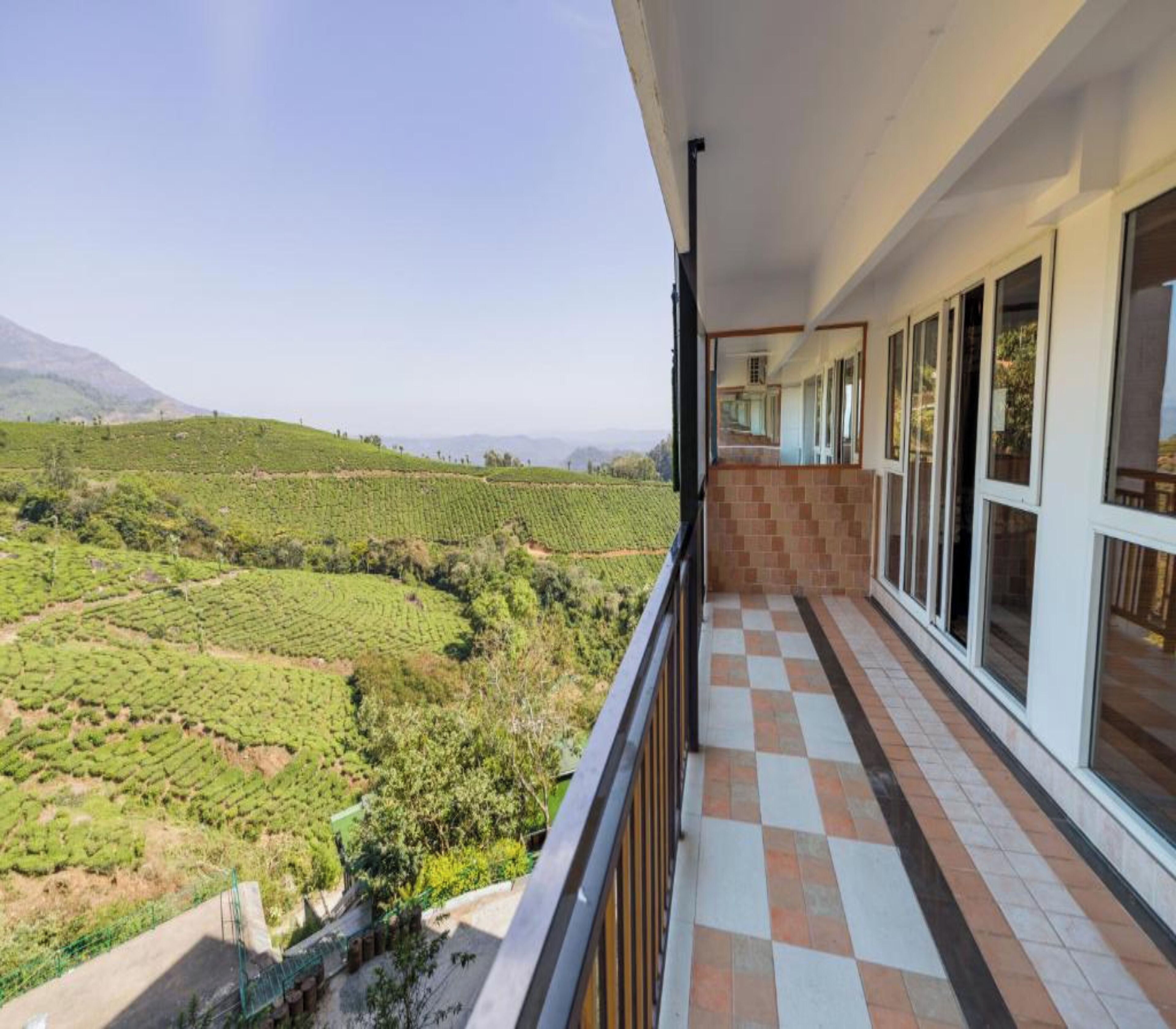 A balcony with a checkered floor, overlooking a tea plantation.