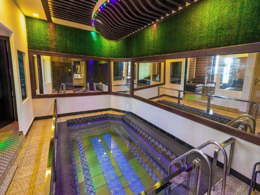Un área de spa con un jacuzzi grande, paredes espejadas y una pared verde con textura.