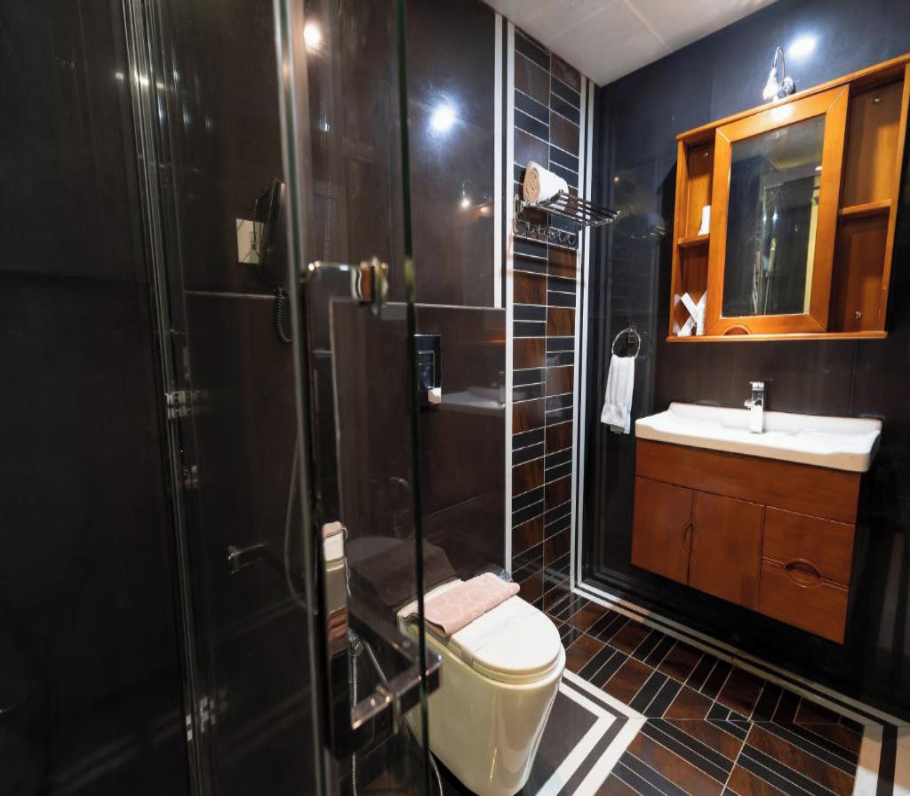 Een moderne badkamer met een douchecabine van glas, een houten wastafelmeubel en een vloer van zwart tegels.