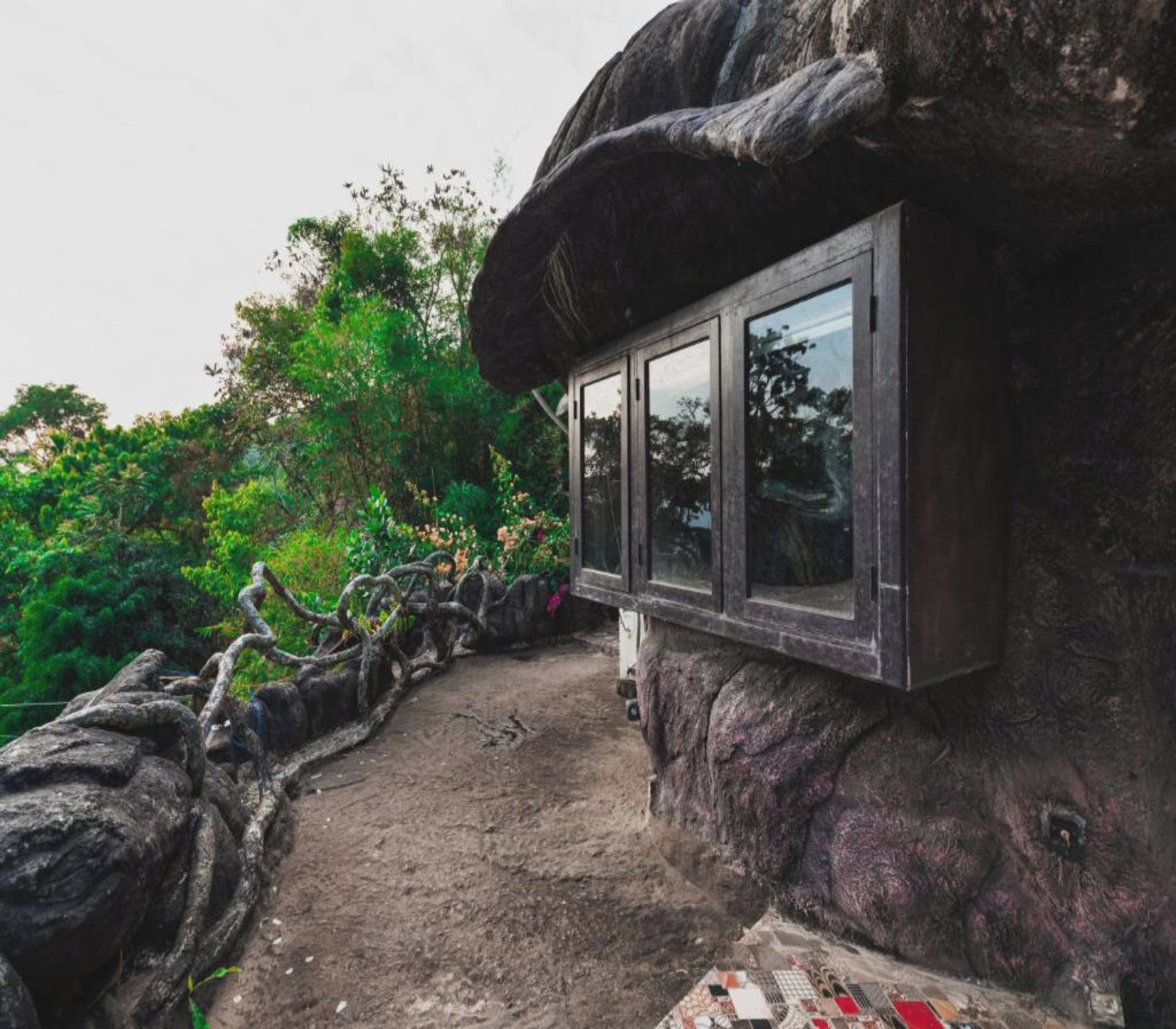 A rustic, stone structure with a window, surrounded by lush greenery and a dirt path.