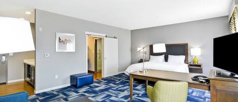 A hotel room with a bed, desk, chair, and a television.